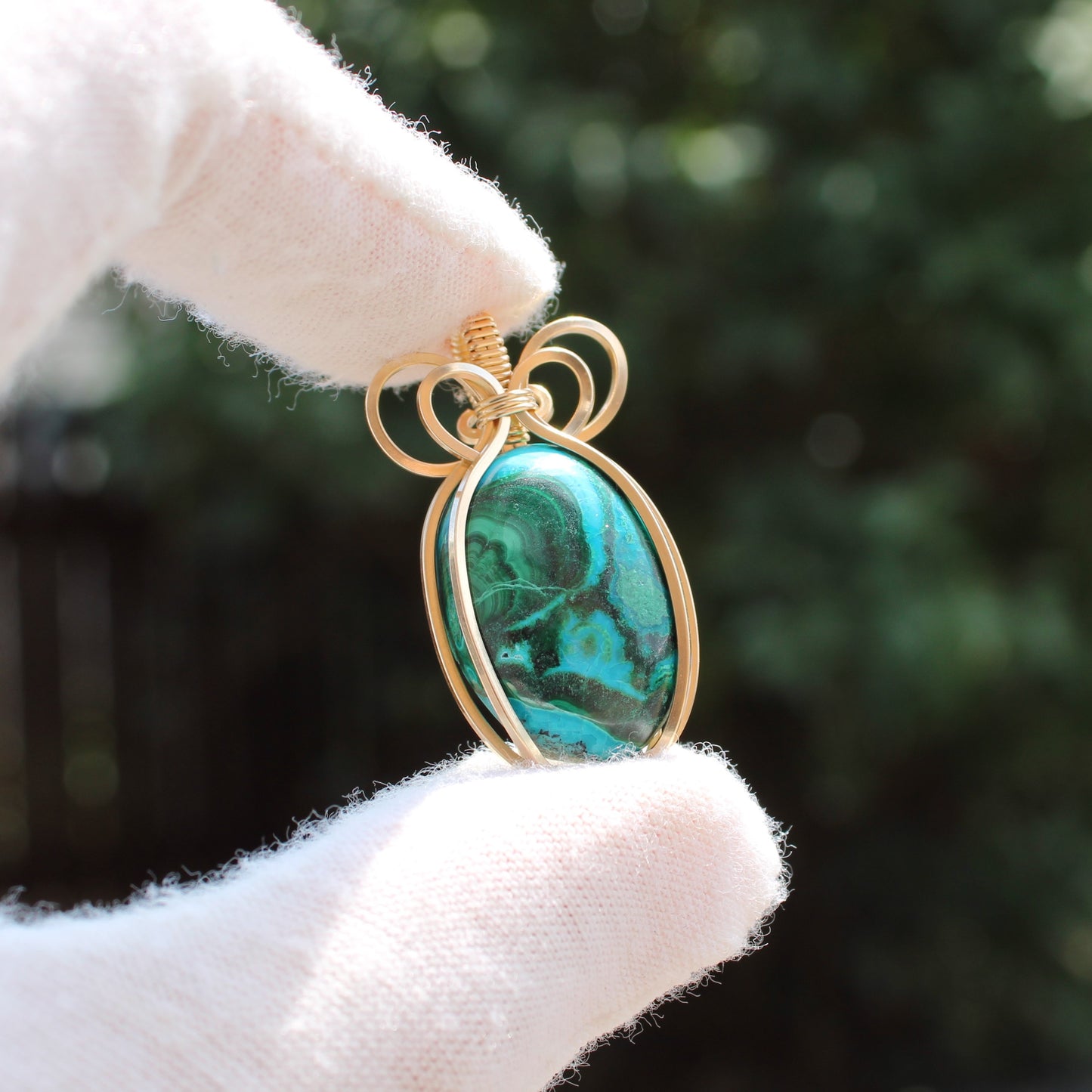 14k Gold Filled Chrysocolla Malachite pendant with gold wire wrapping held between gloved fingers