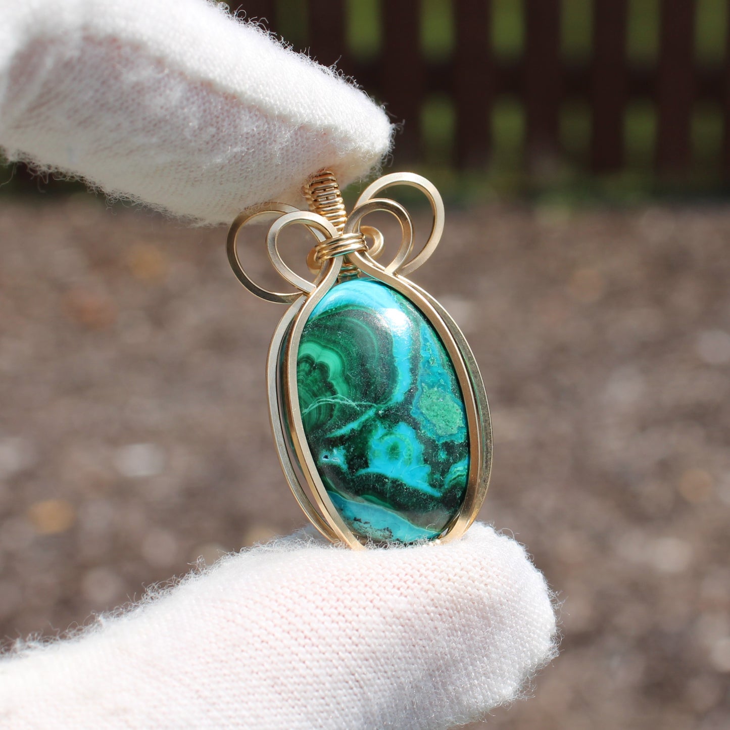 14k Gold Filled Chrysocolla Malachite pendant with blue and green stone held by gloved hand