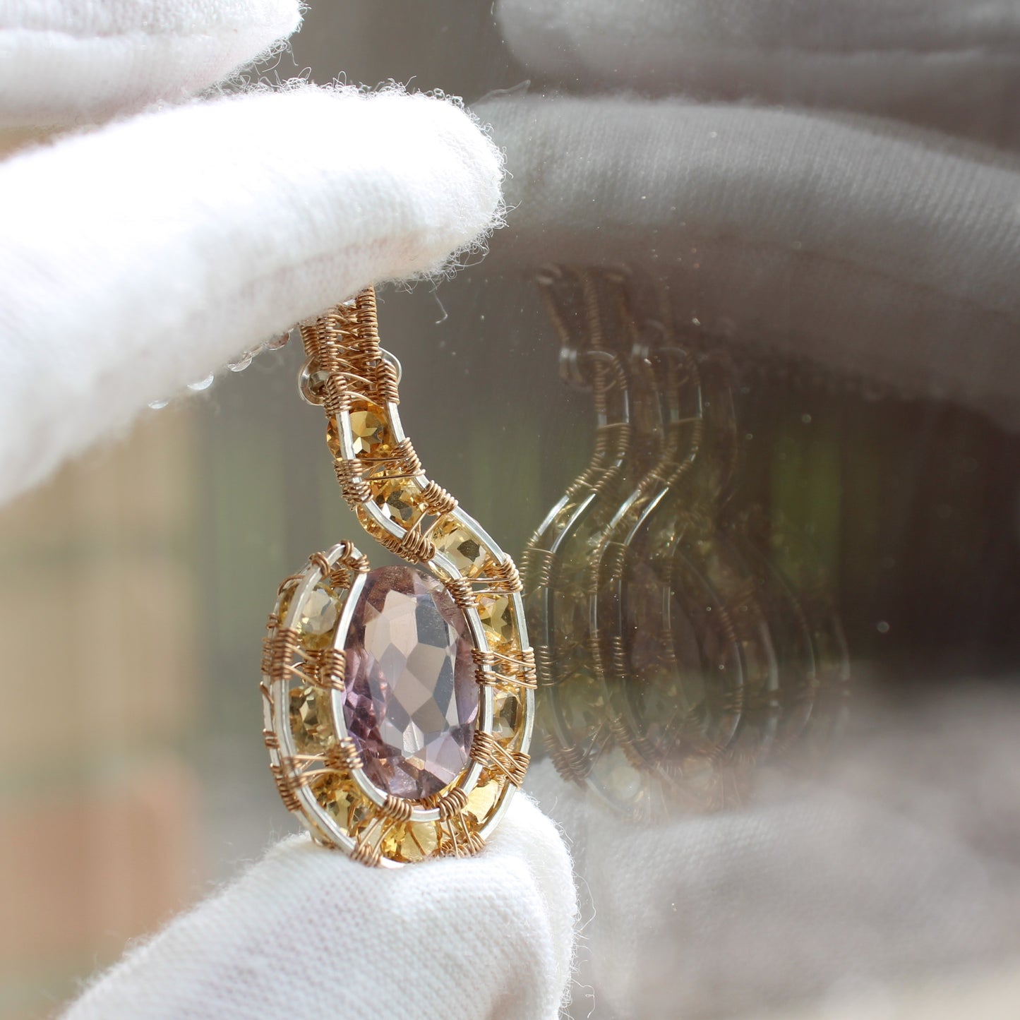 Intricately designed amethyst citrine pendant highlighted against a reflective surface