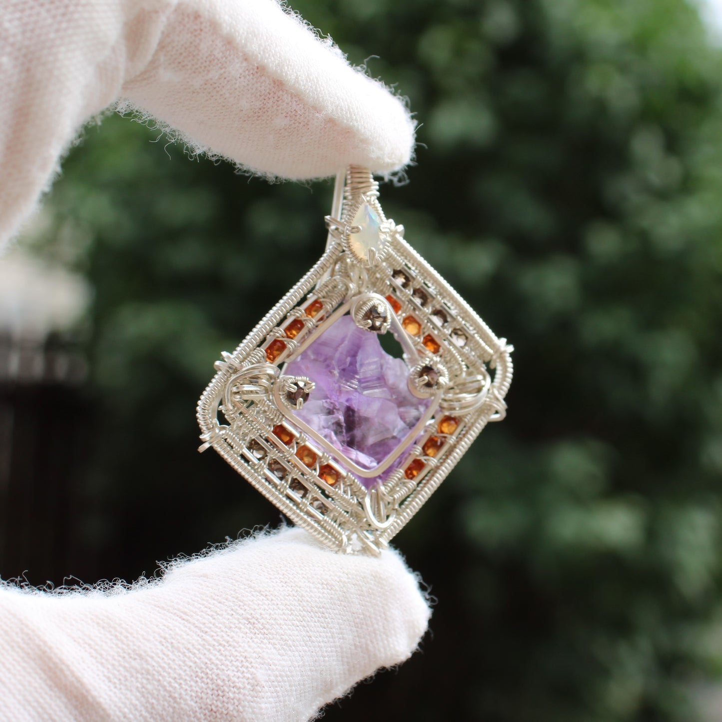 Hand holding Different Branches LLC jewelry featuring amethyst garnet opal silver wire wrapped pendant