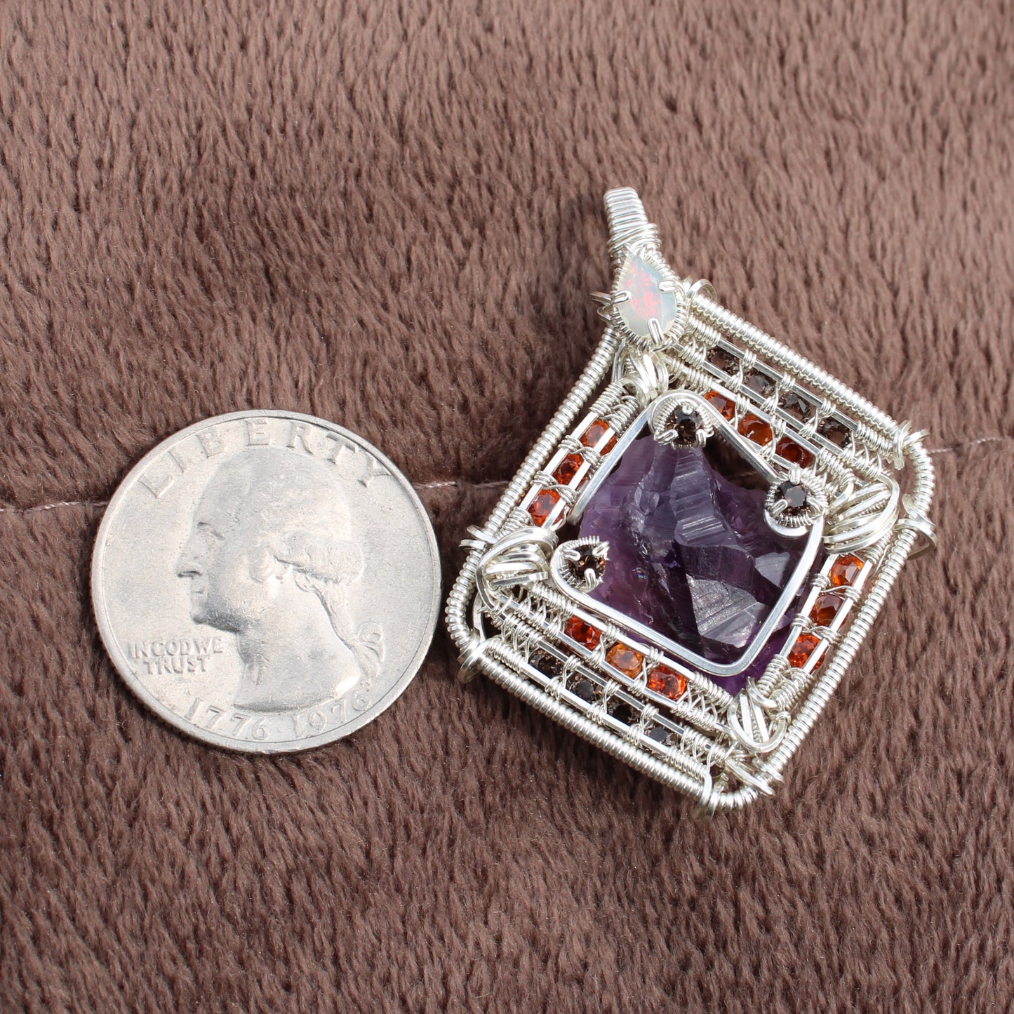 Amethyst garnet opal silver wire-wrapped pendant jewelry piece next to a quarter for size comparison