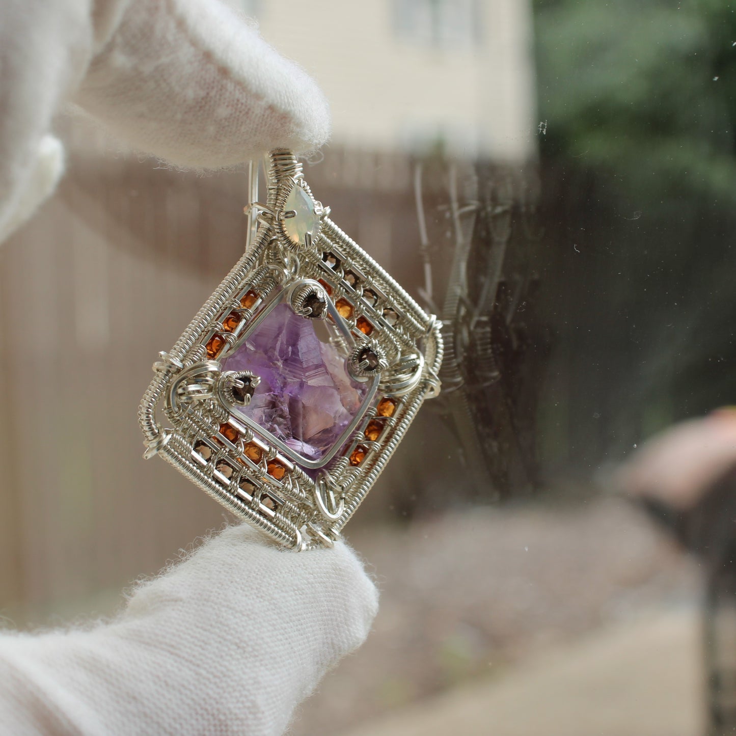 Hand holding amethyst garnet opal silver wire-wrapped intricate square pendant jewelry