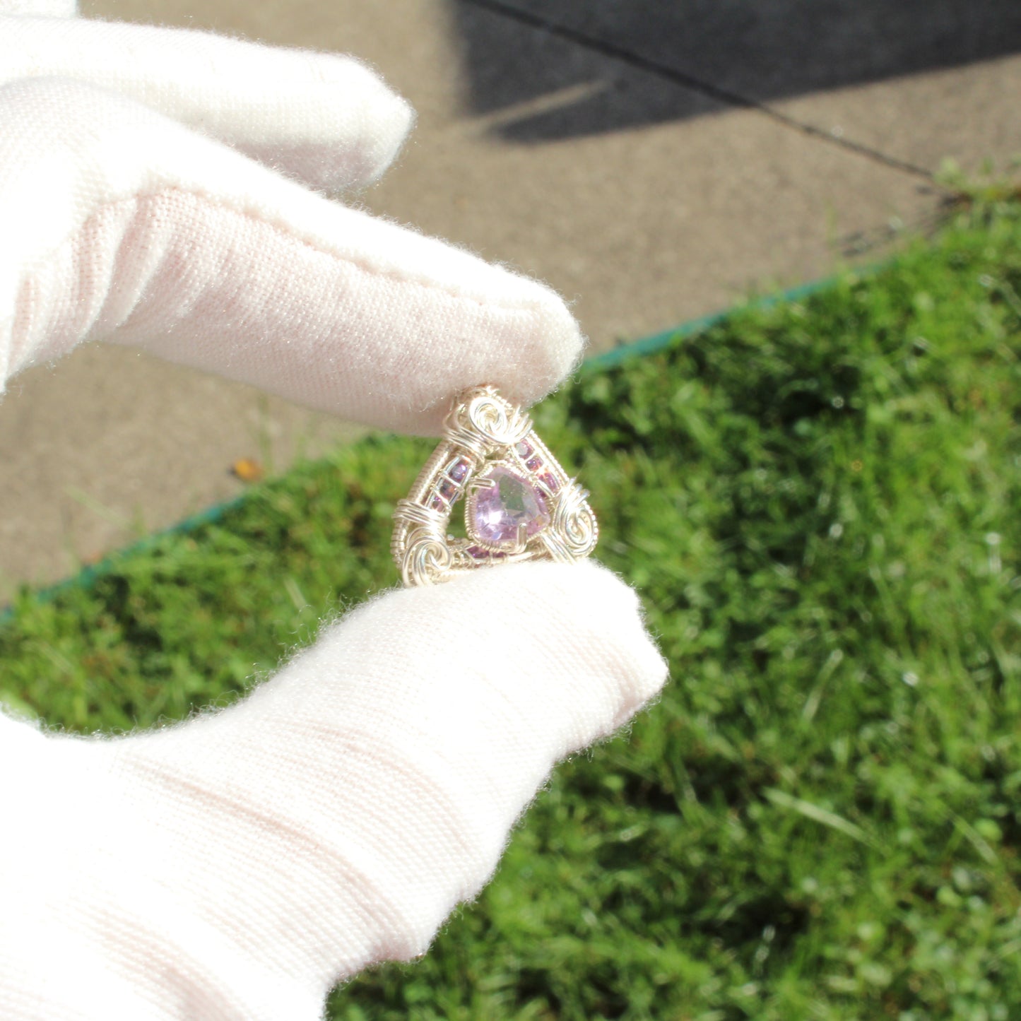 Amethyst set in sterling silver pendant held by a gloved hand against a green background