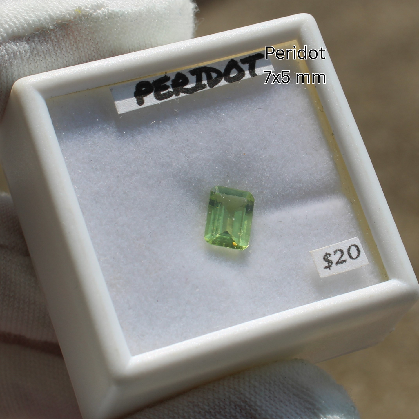 Peridot crystal 7x5 mm emerald cut in white display box labeled 20 dollars for Made to order rings