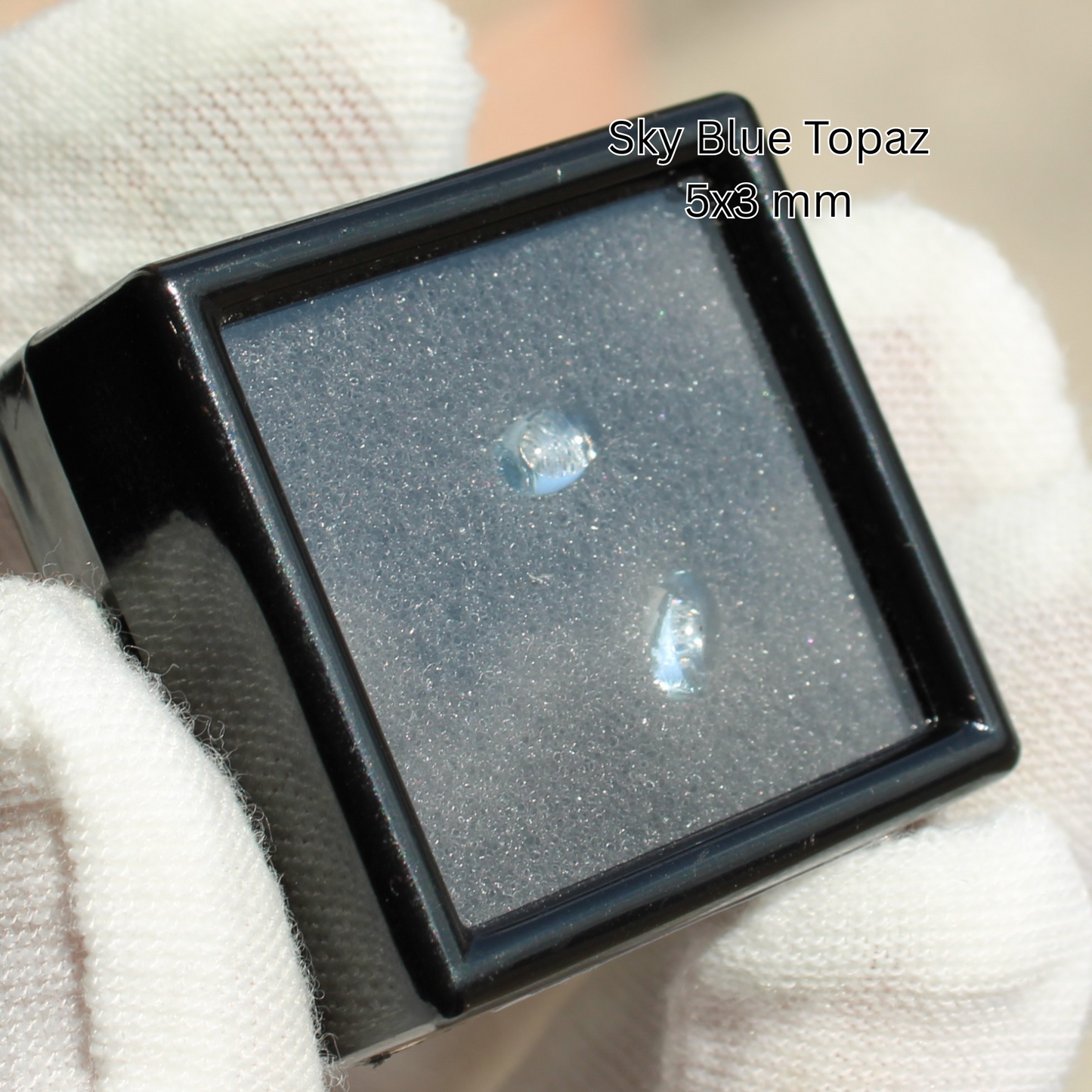 Two sky blue topaz crystals 5x3 mm in black display box held by white glove for Made to order rings
