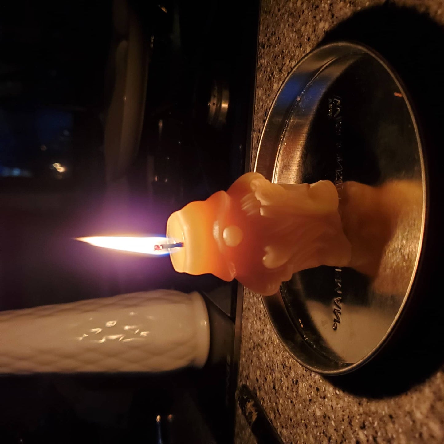 Beeswax gnome candle glowing with a flame on a silver plate in a cozy setting