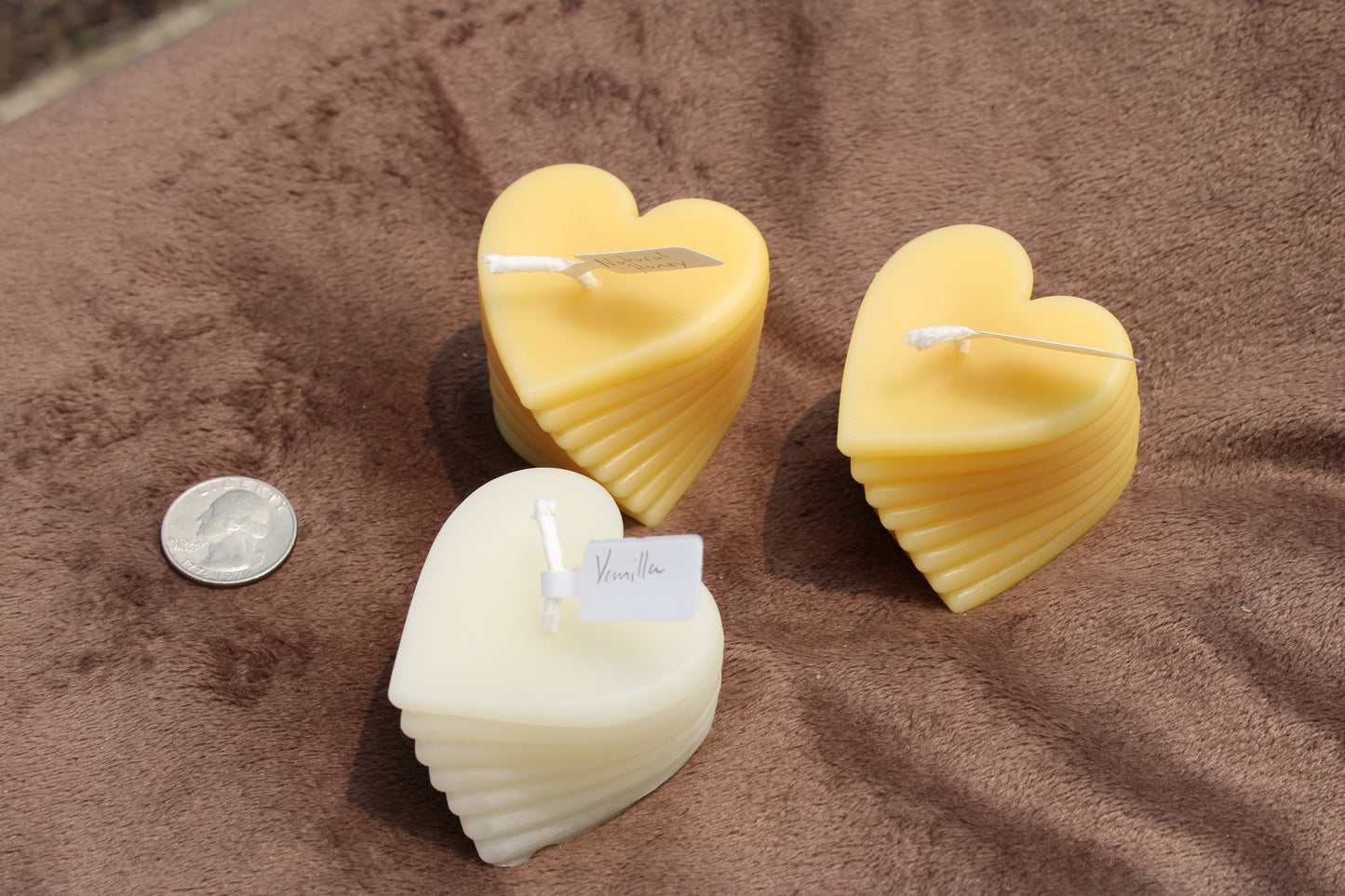 Three My Store beeswax heart candles in yellow and white stacked together with a coin for size reference