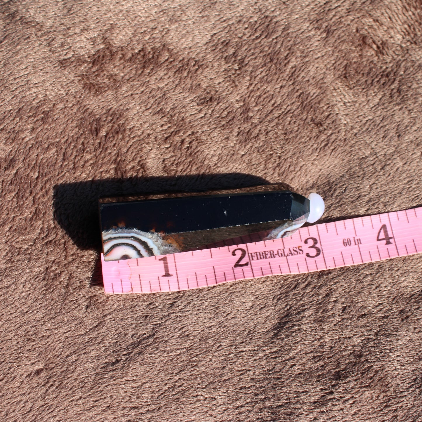 Black Agate Tower Collection featuring a polished crystal with natural patterns and a measuring tape for scale