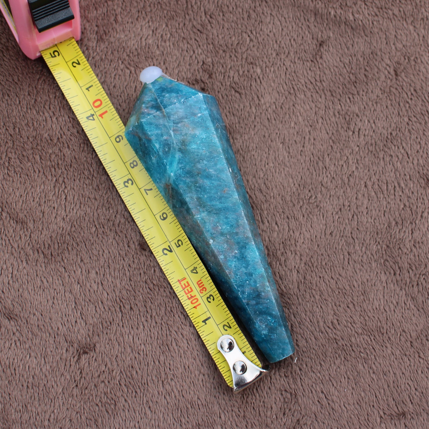 Blue Apatite Wand crystal measuring about 4 inches on a brown fabric surface
