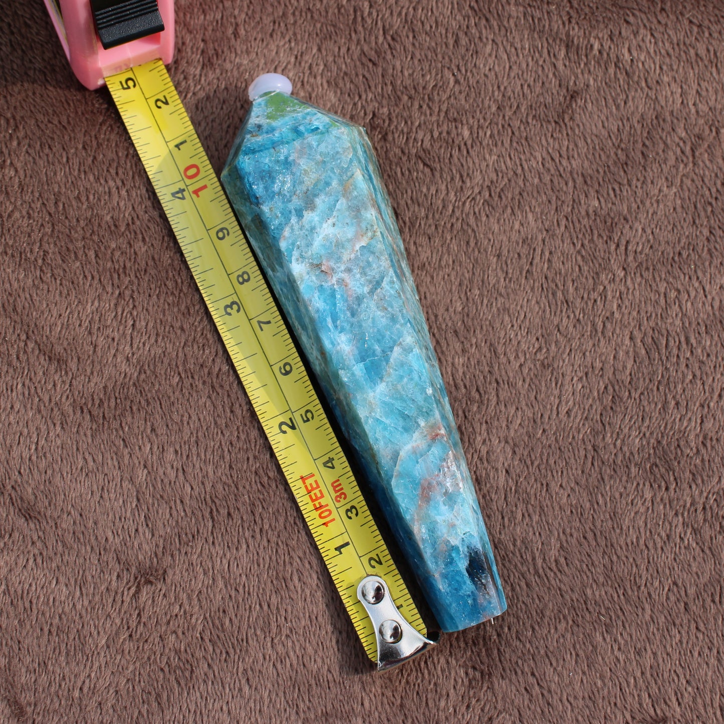 Blue Apatite Wand crystal placed next to yellow measuring tape on brown fabric background