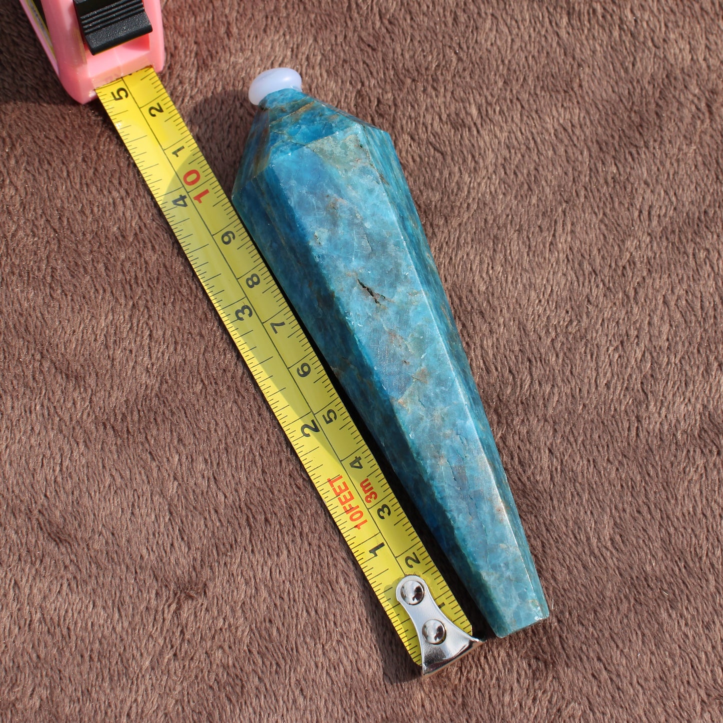 Blue Apatite Wand crystal from Different Branches LLC next to measuring tape on brown fabric