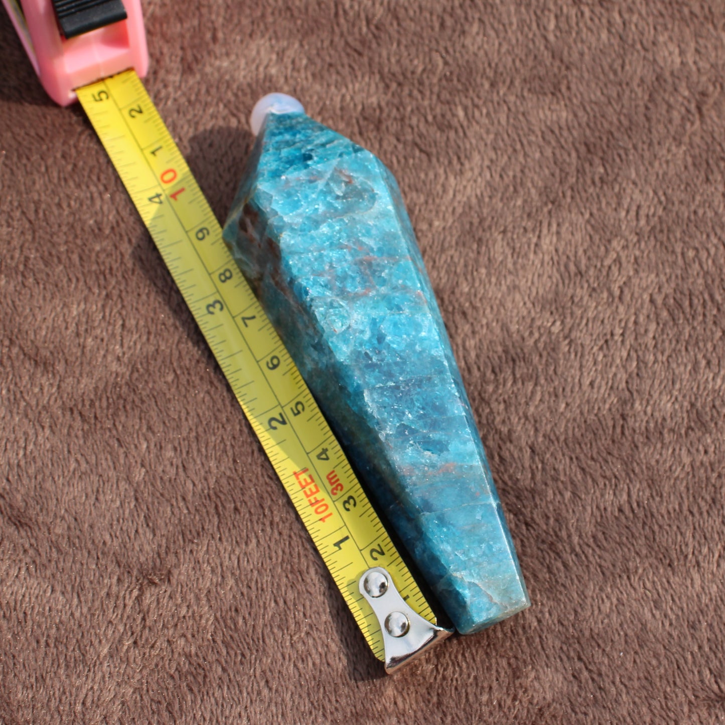 Blue Apatite Wand crystal next to measuring tape on brown fabric showing size and texture