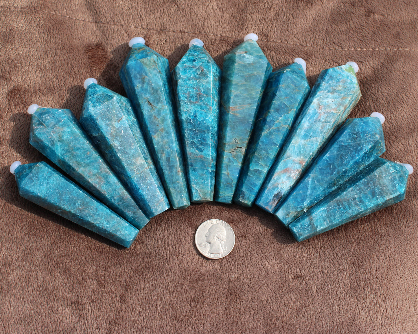 Set of polished Blue Apatite Wand crystals from Different Branches LLC displayed on brown fabric with a quarter for size reference