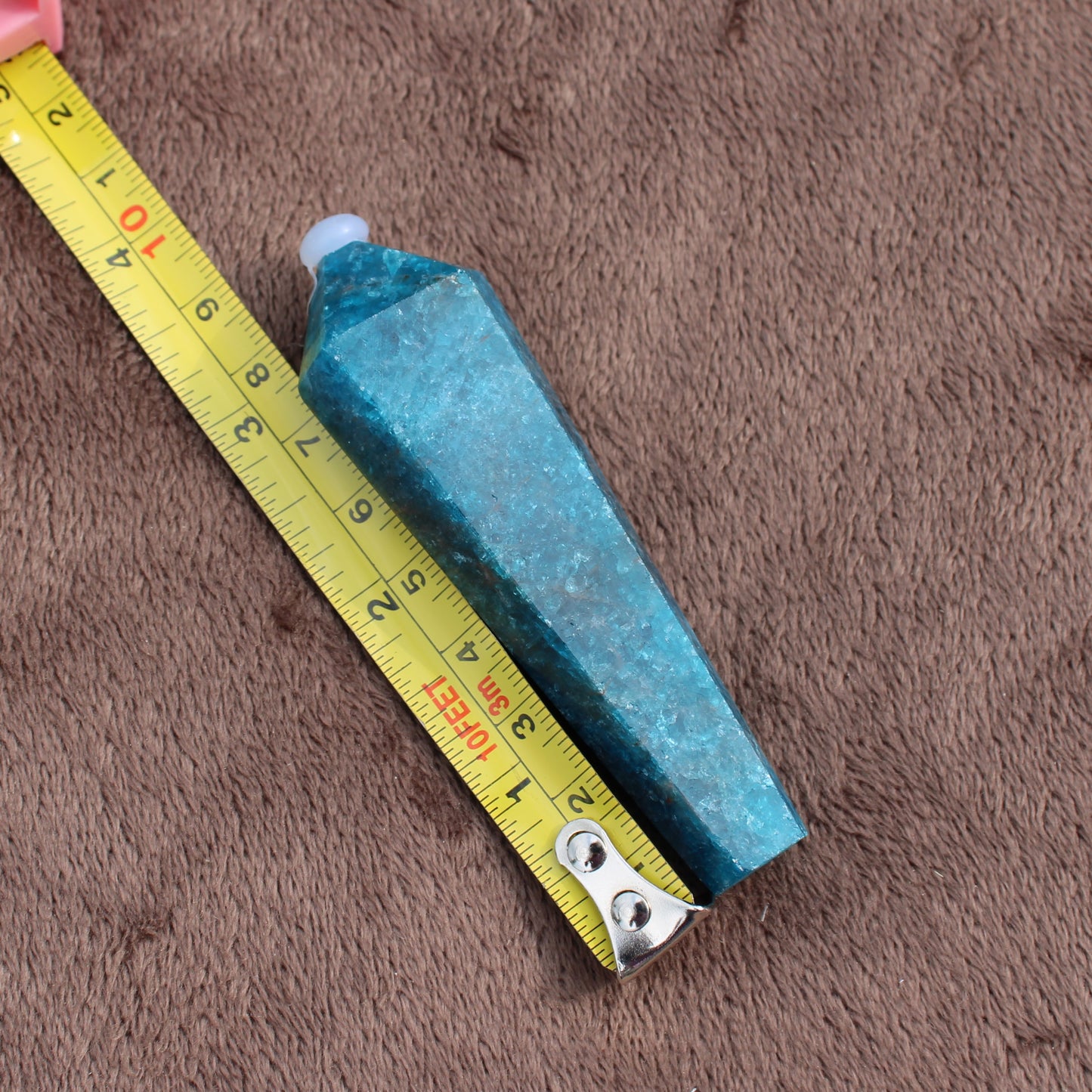 Blue Apatite Wand crystal next to measuring tape showing its length on brown fabric background