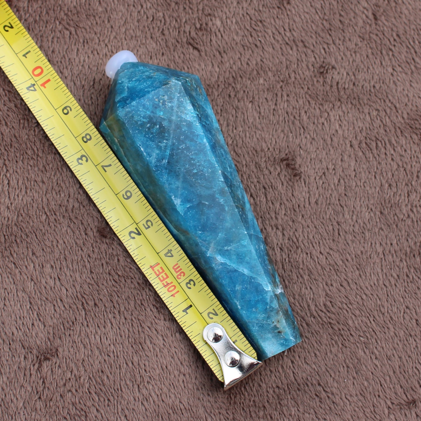 Blue Apatite Wand crystal from Different Branches LLC placed next to a tape measure on brown fabric