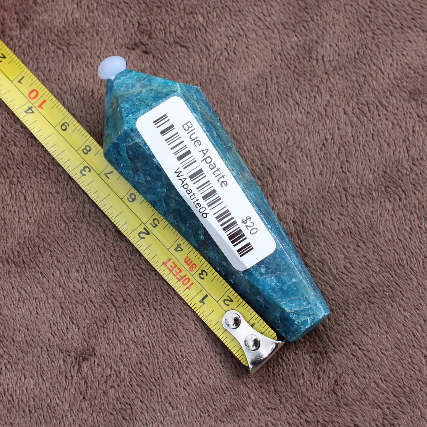 Blue Apatite Wand crystal measuring about 4 inches with price label on a brown textured surface