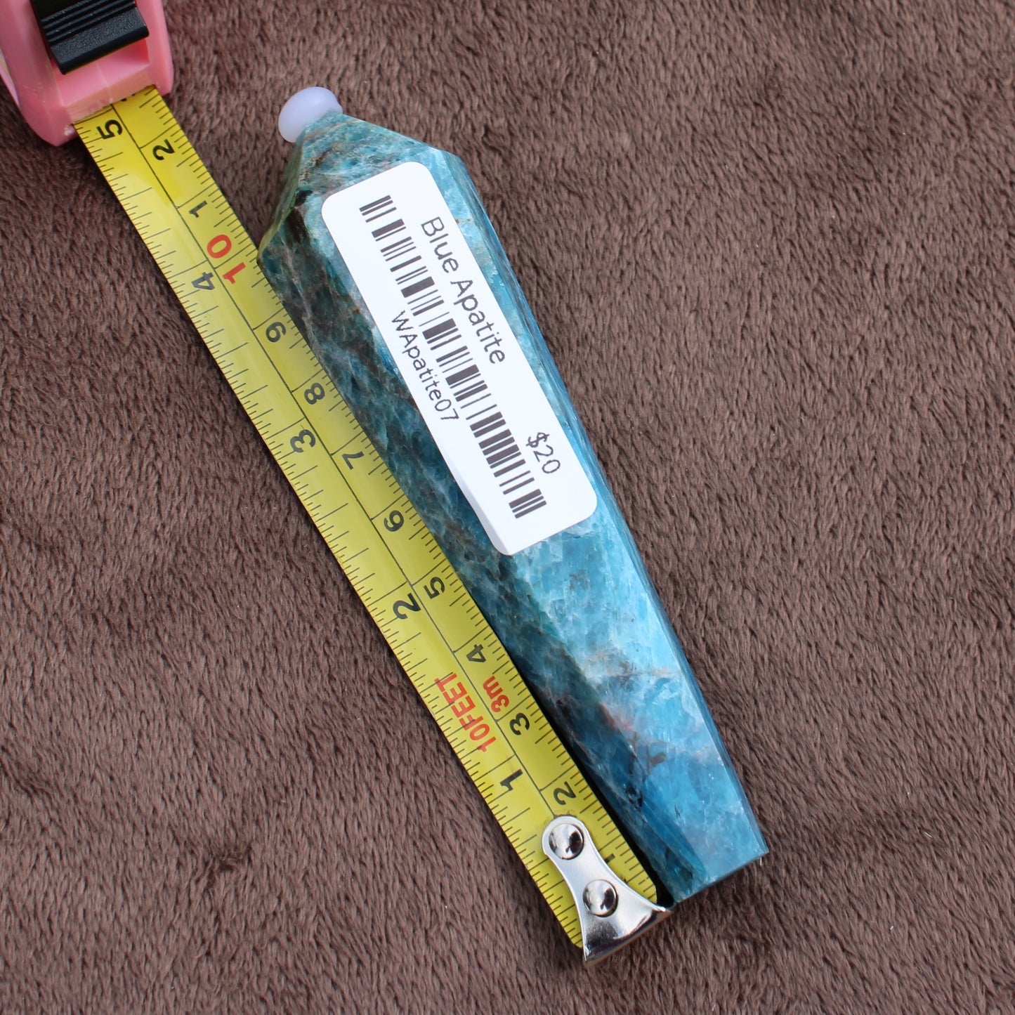 Blue Apatite Wand crystal measuring approximately 5 inches on a yellow tape measure