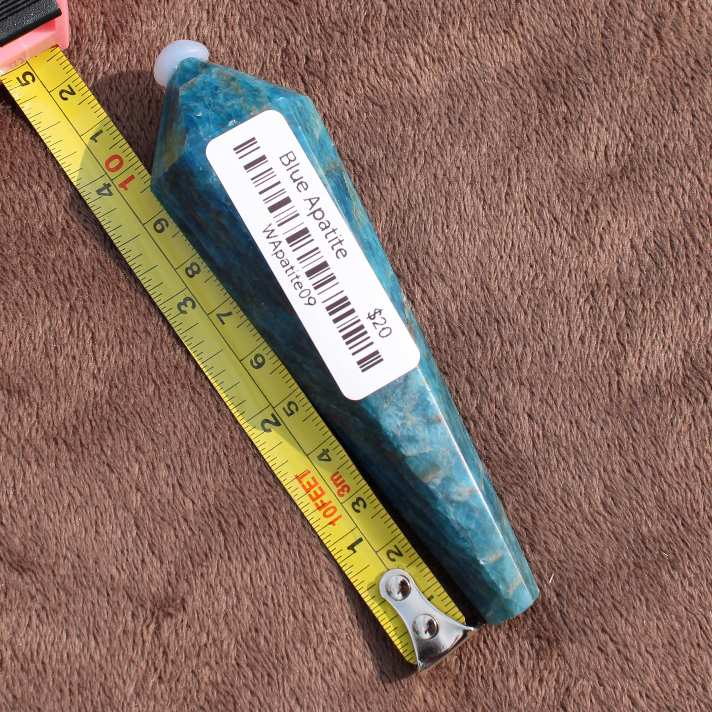 Blue Apatite Wand crystal from Different Branches LLC placed next to a tape measure on a brown surface