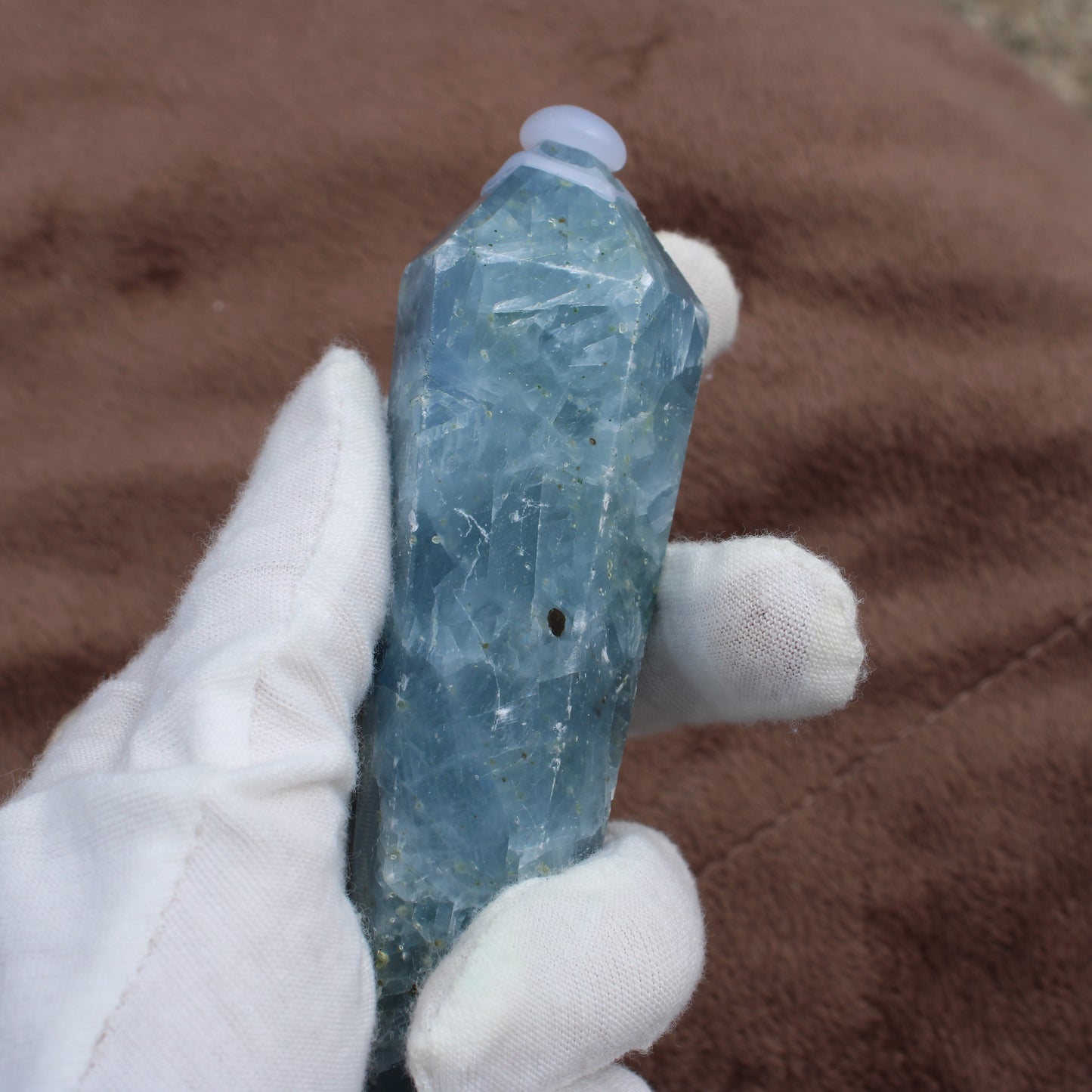Blue Calcite Wand crystal held in white gloved hand showing its smooth polished surface