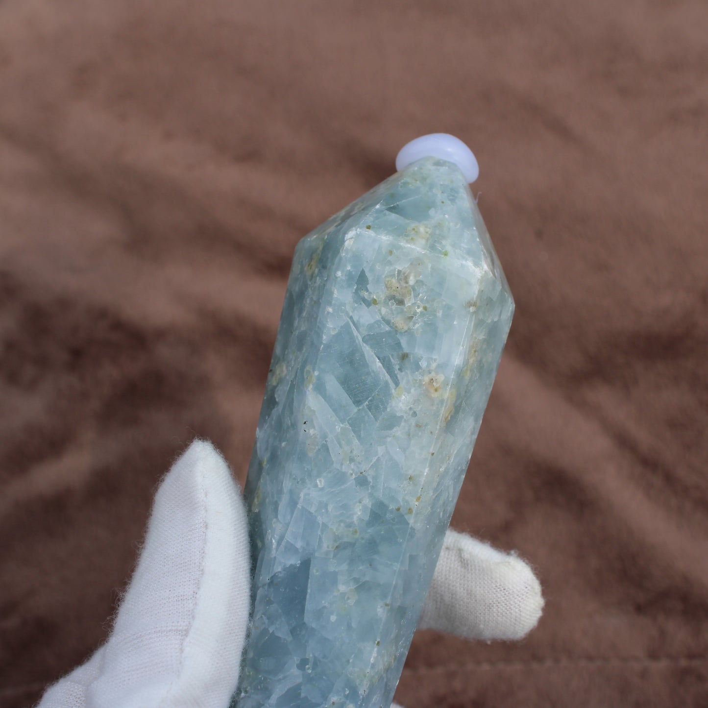 Blue Calcite Wand crystal held in white glove showing its translucent blue tones and natural texture