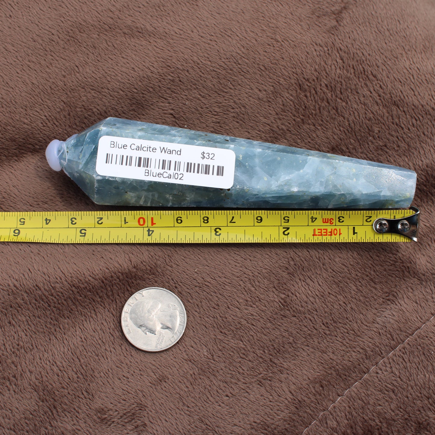 Blue Calcite Wand from Different Branches LLC next to measuring tape and coin for size reference