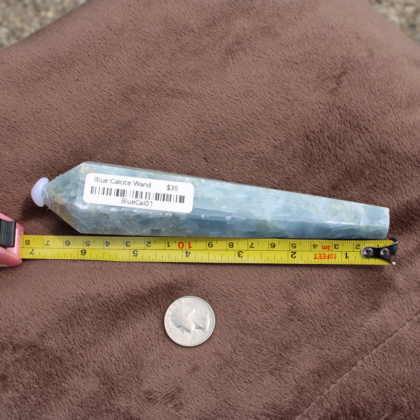 Blue Calcite Wand measuring about 6 inches placed next to a tape measure and a quarter coin