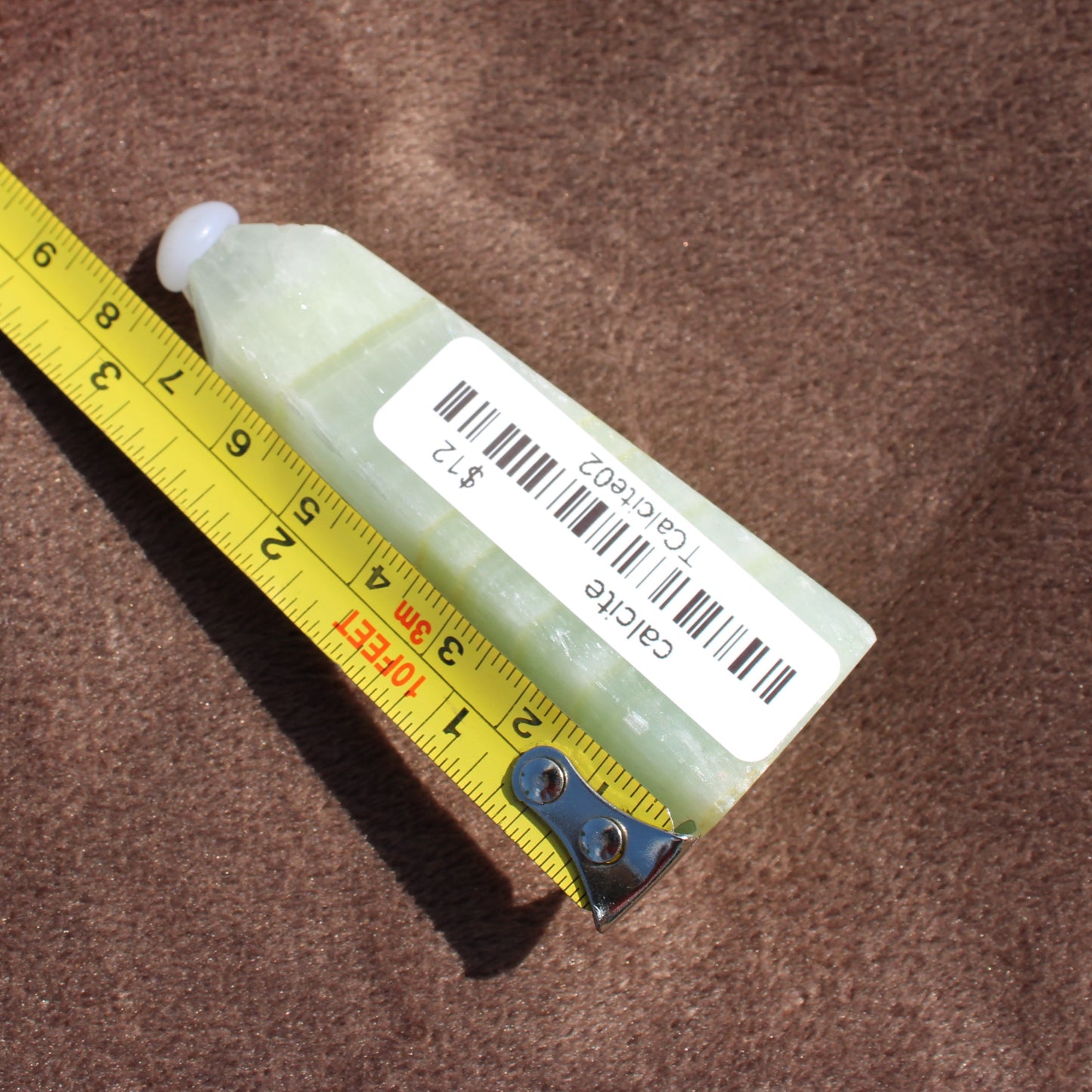 Calcite Tower crystal from Different Branches LLC shown next to measuring tape on brown surface