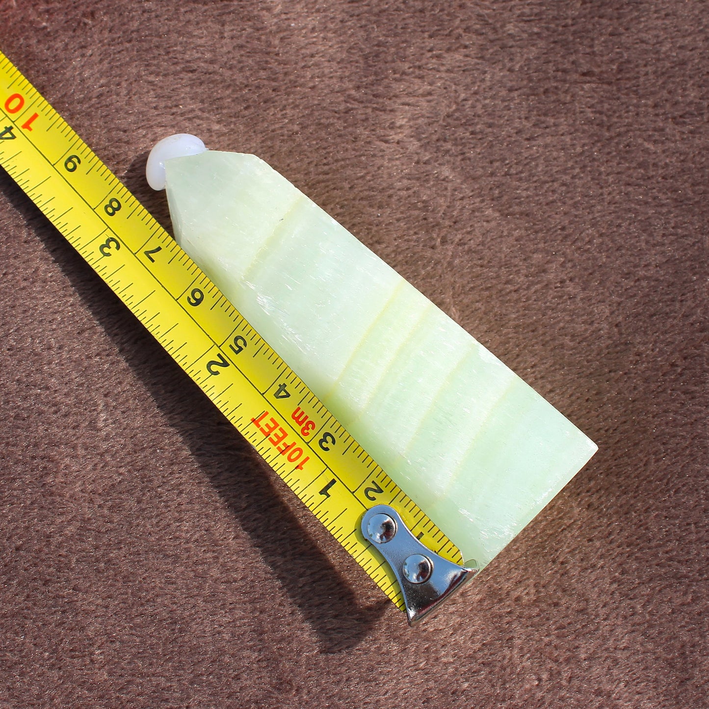 Light green Calcite Tower crystal next to a measuring tape showing size on brown surface