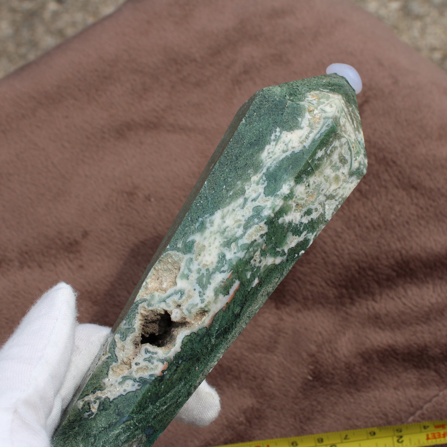 Green and white polished Moss Agate Wand held by gloved hand on brown background