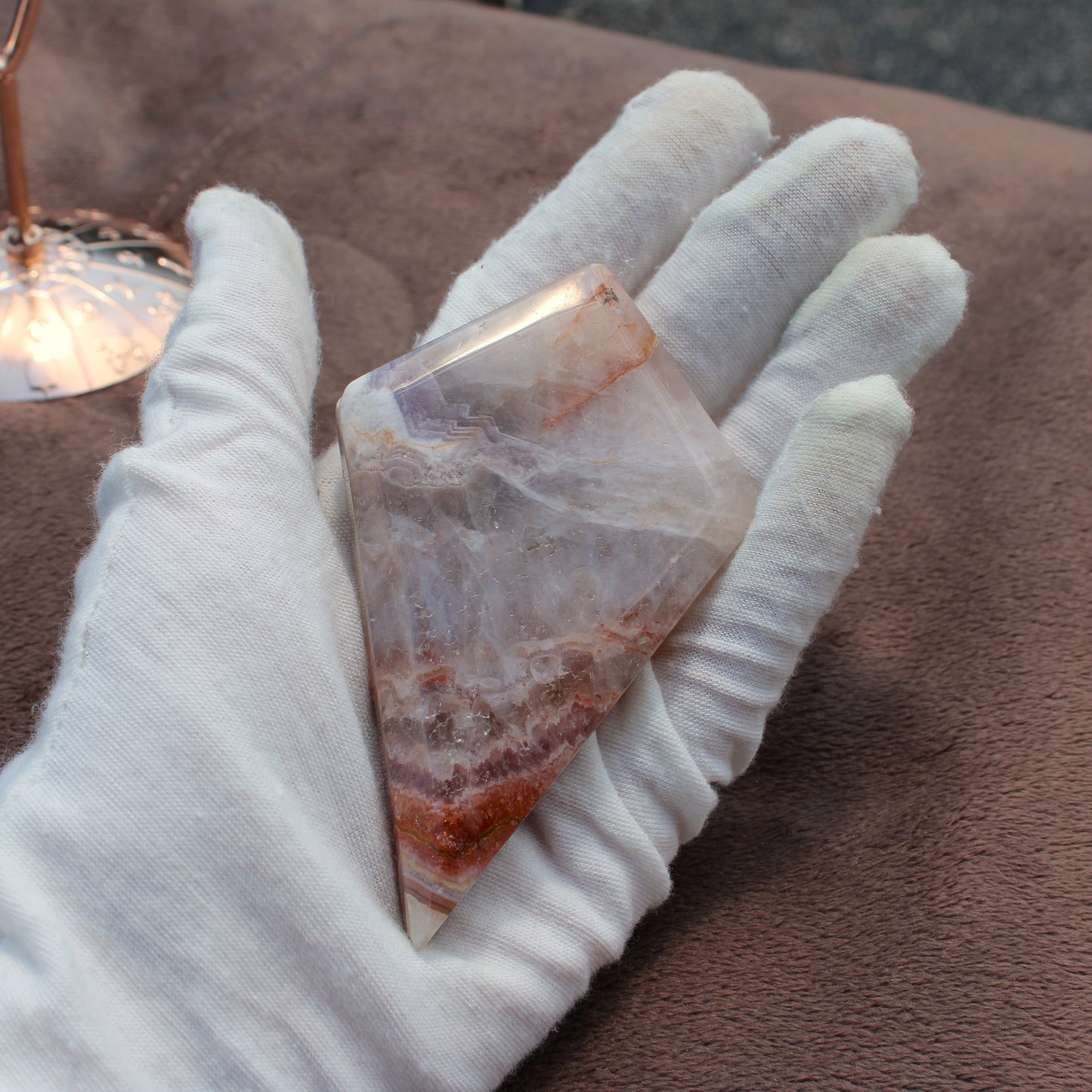 Hand holding a polished Crazy Lace Agate Diamond crystal with white and reddish brown patterns