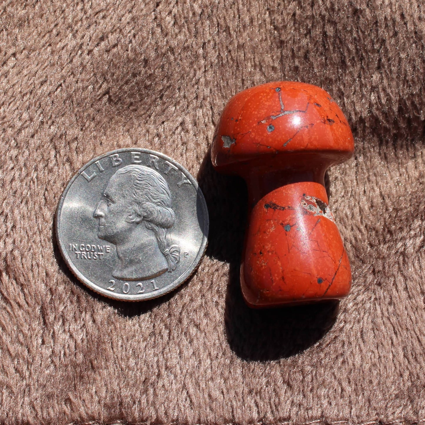 Beautiful red Crystal Mushroom Carving next to a quarter for size comparison