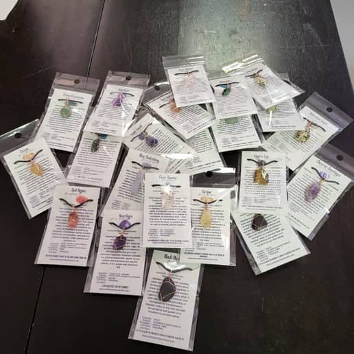 Variety of crystal necklaces with info cards displayed on a dark table for jewelry enthusiasts