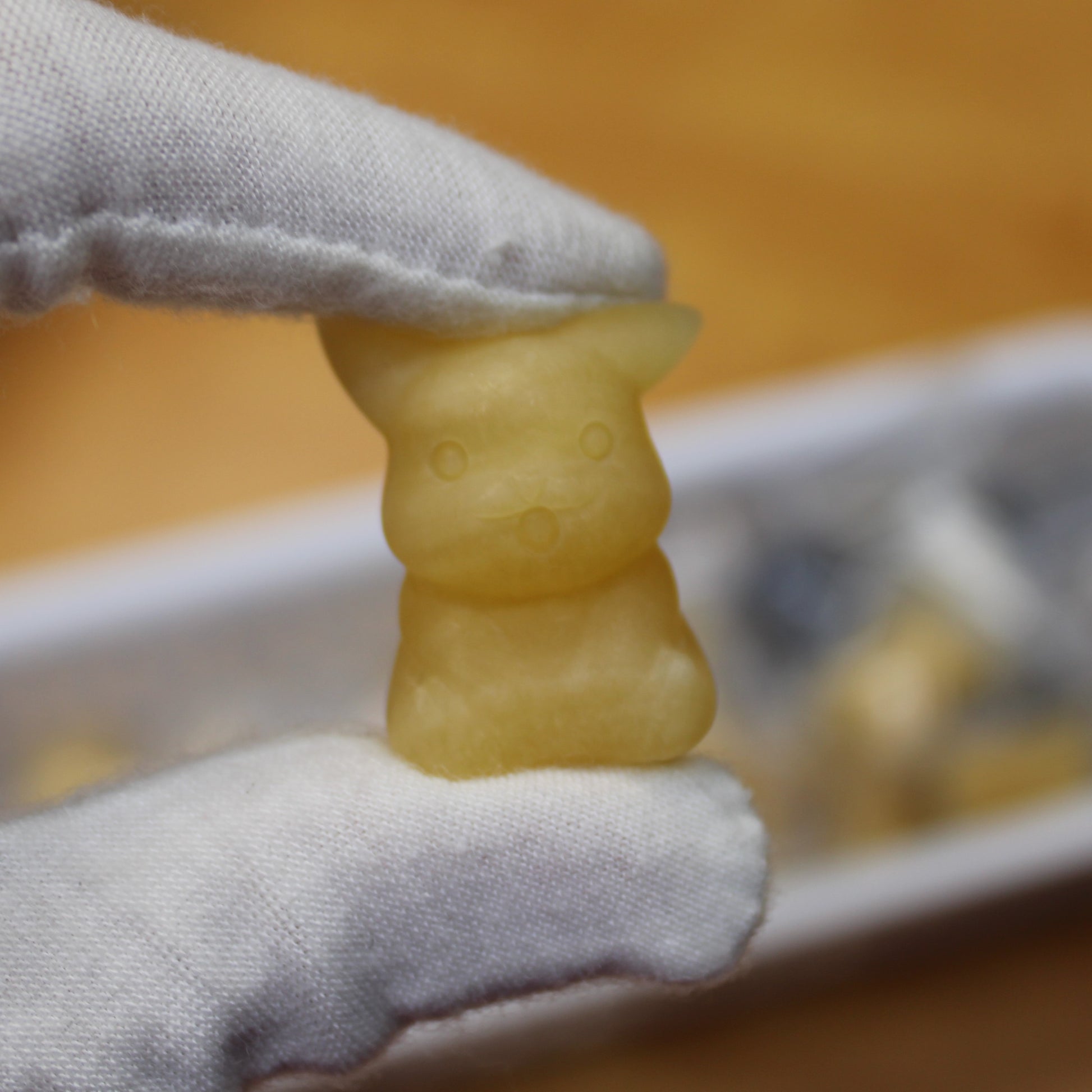 Close-up of a yellow crystal Pikachu figurine from crystal pokemon gift set held by white gloved hand