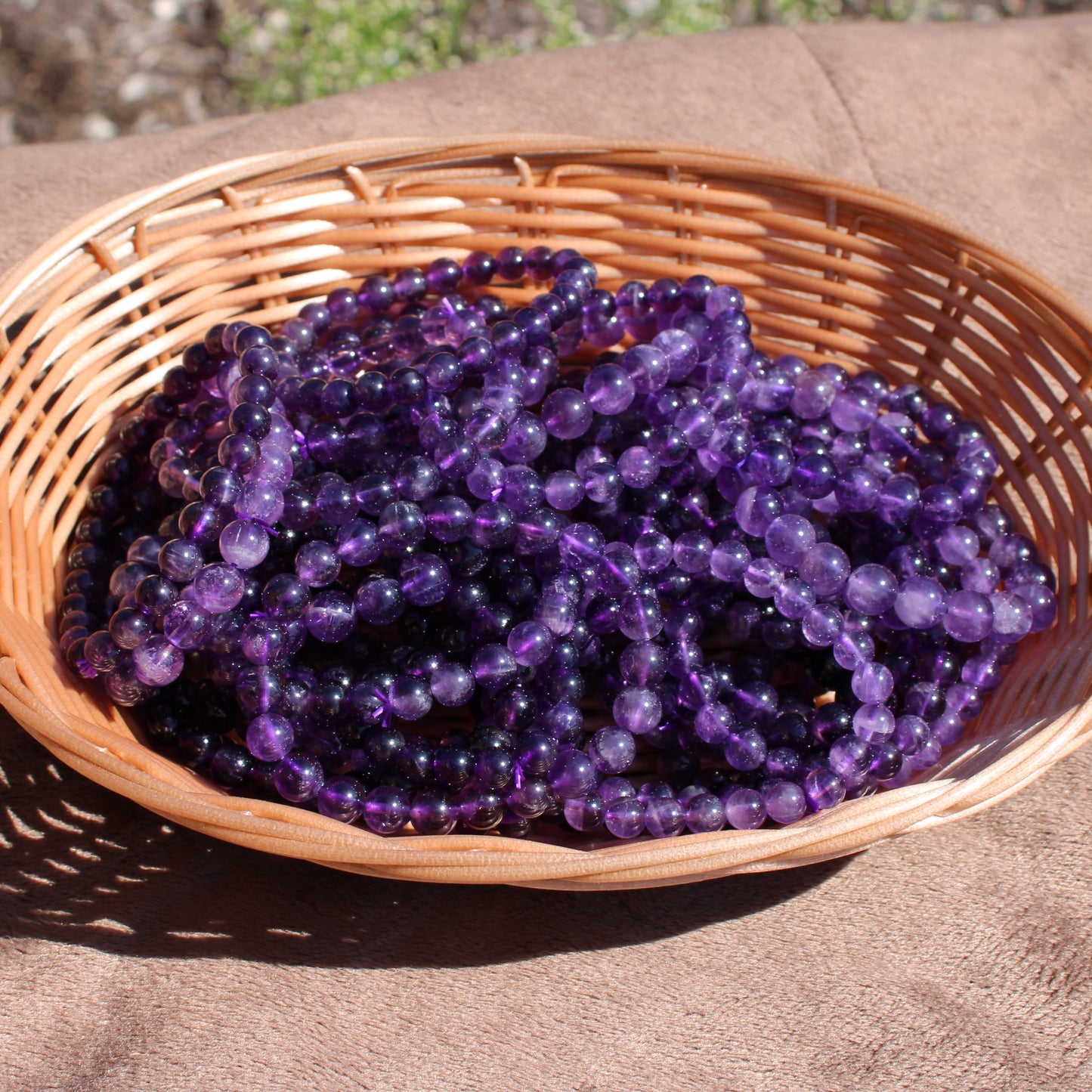 Deep Purple Amethyst Bracelet strands arranged in a woven basket on a sunny surface