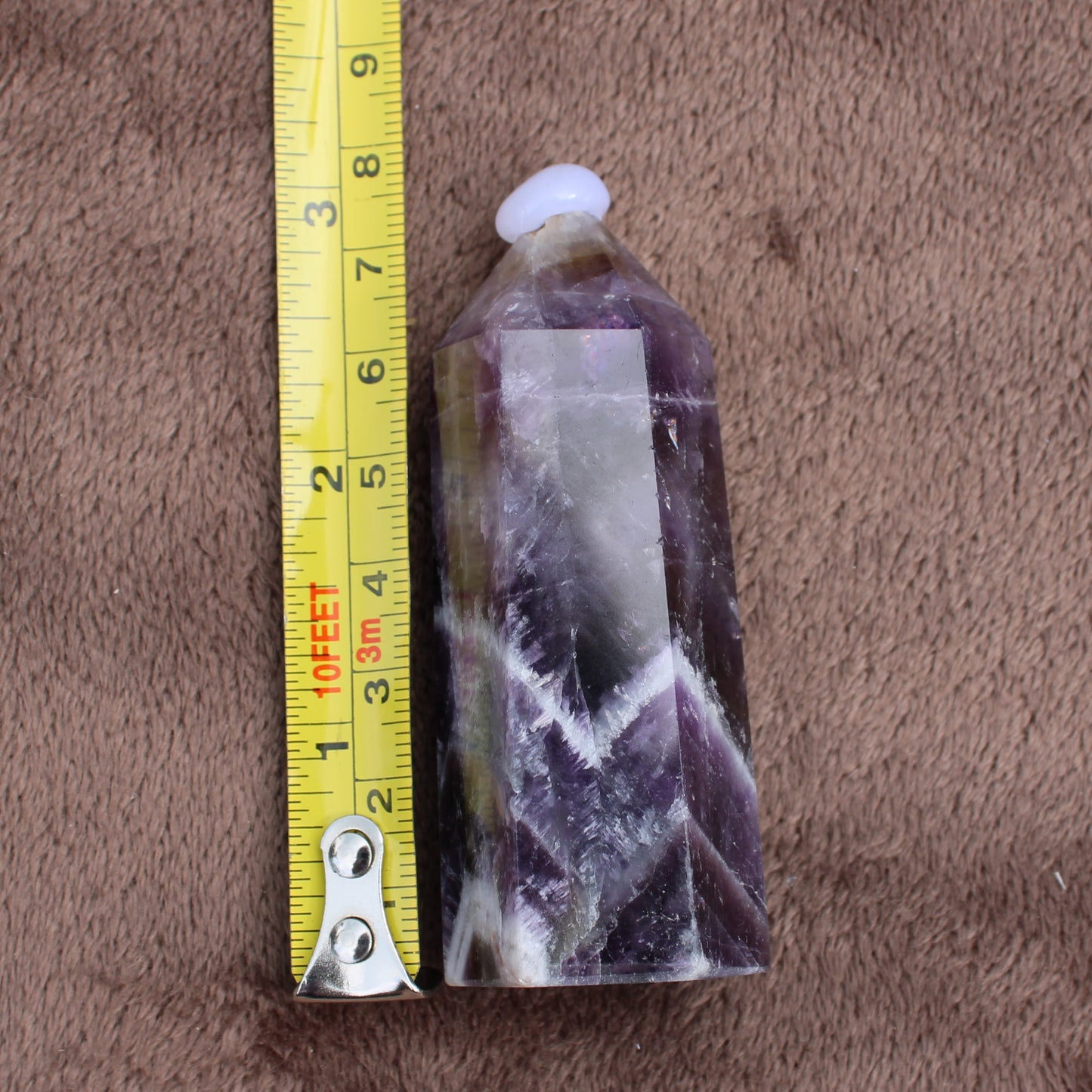 Dream Amethyst Tower crystal standing next to a measuring tape showing size on a brown fabric background