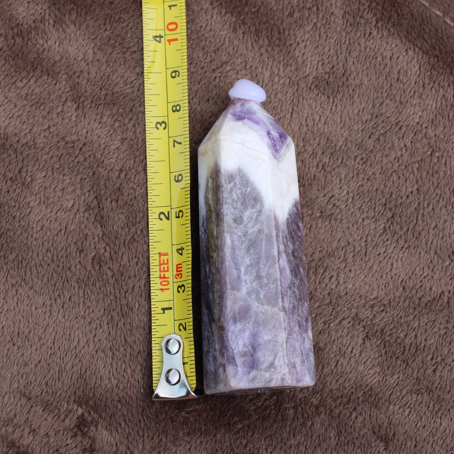 Dream Amethyst Tower crystal standing next to measuring tape showing its size on a brown fabric background