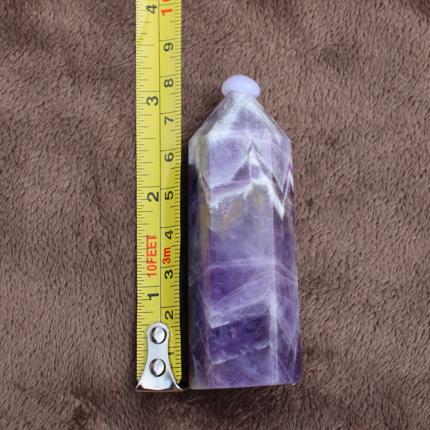 Dream Amethyst Tower crystal beside measuring tape on brown fabric background