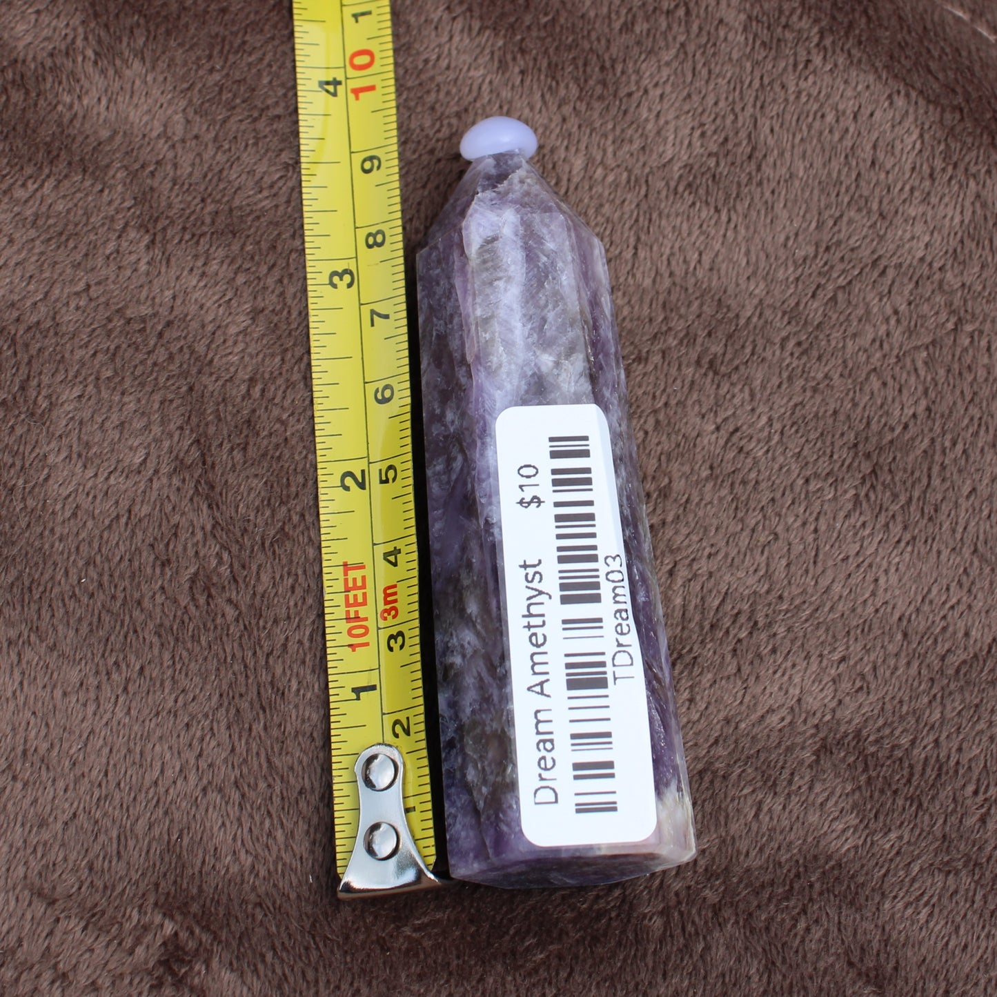 Dream Amethyst Tower crystal with purple hues next to measuring tape showing size on brown fabric