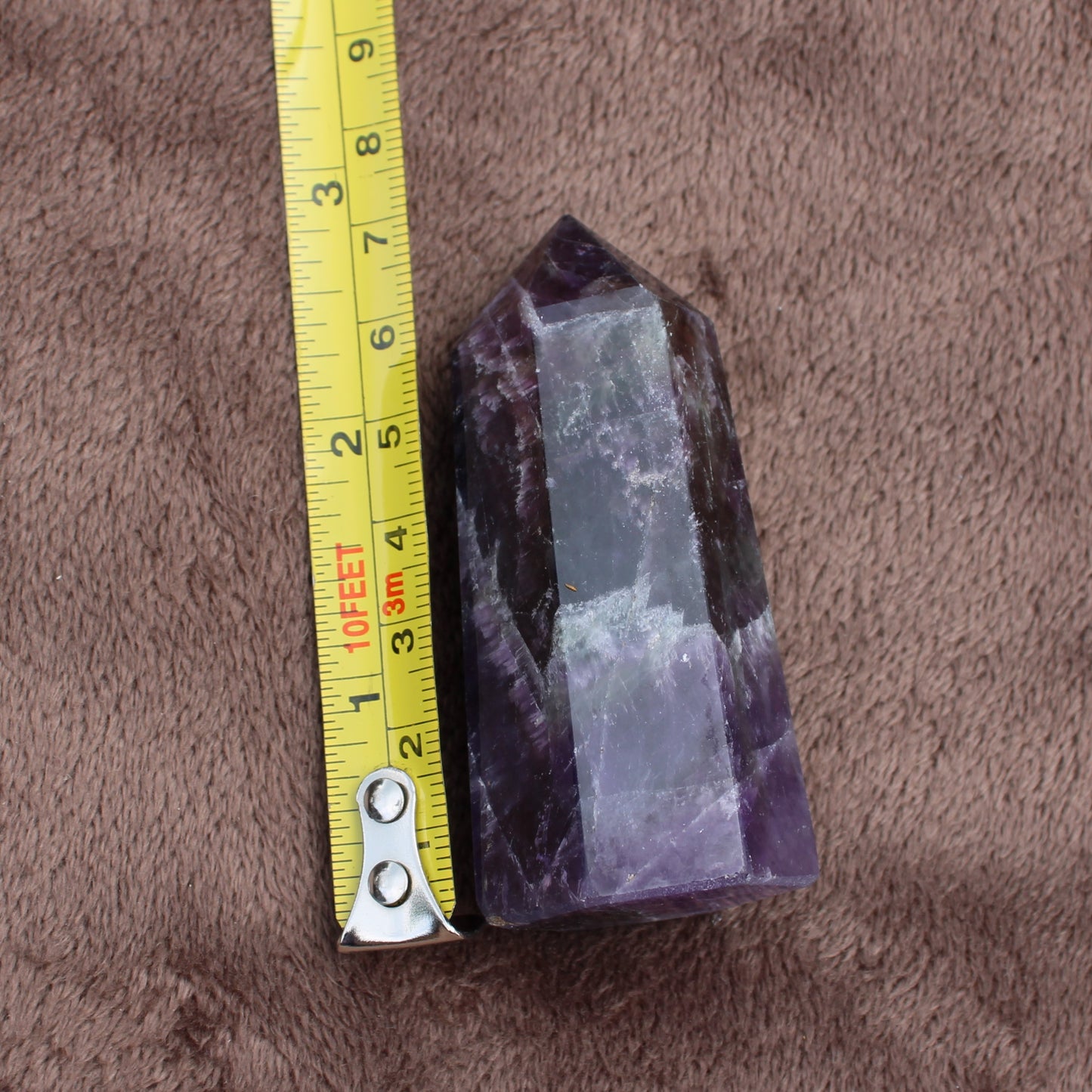 Dream Amethyst Tower crystal standing next to measuring tape on brown