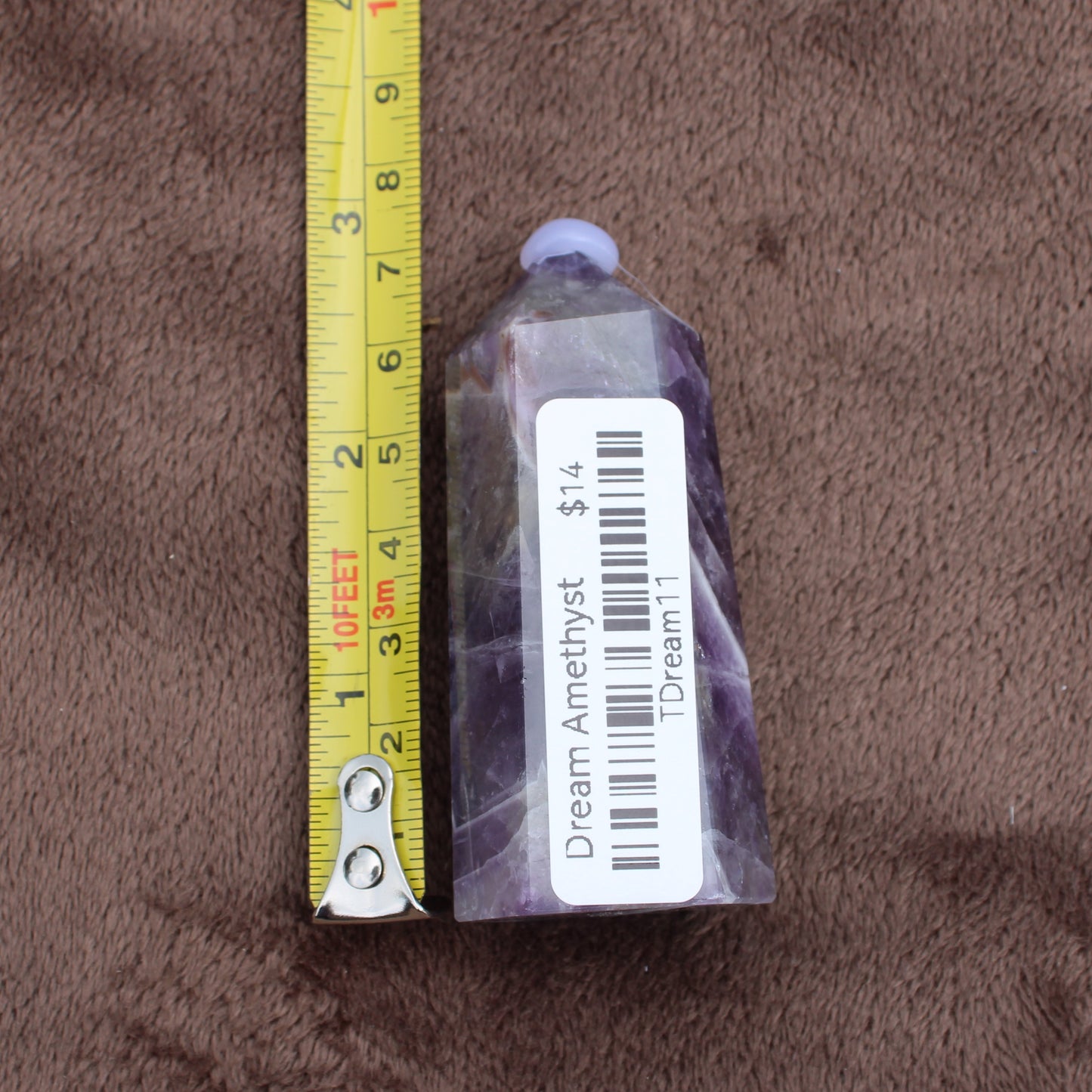 Dream Amethyst Tower crystal with purple and white hues next to measuring tape showing size