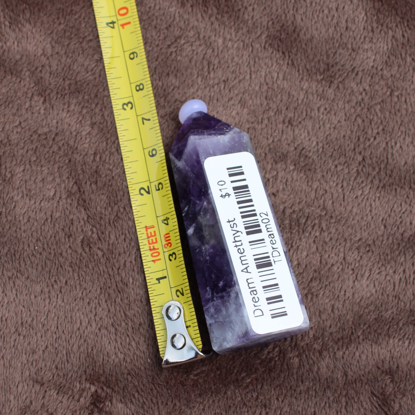 Dream Amethyst Tower crystal next to measuring tape showing size on brown fabric background