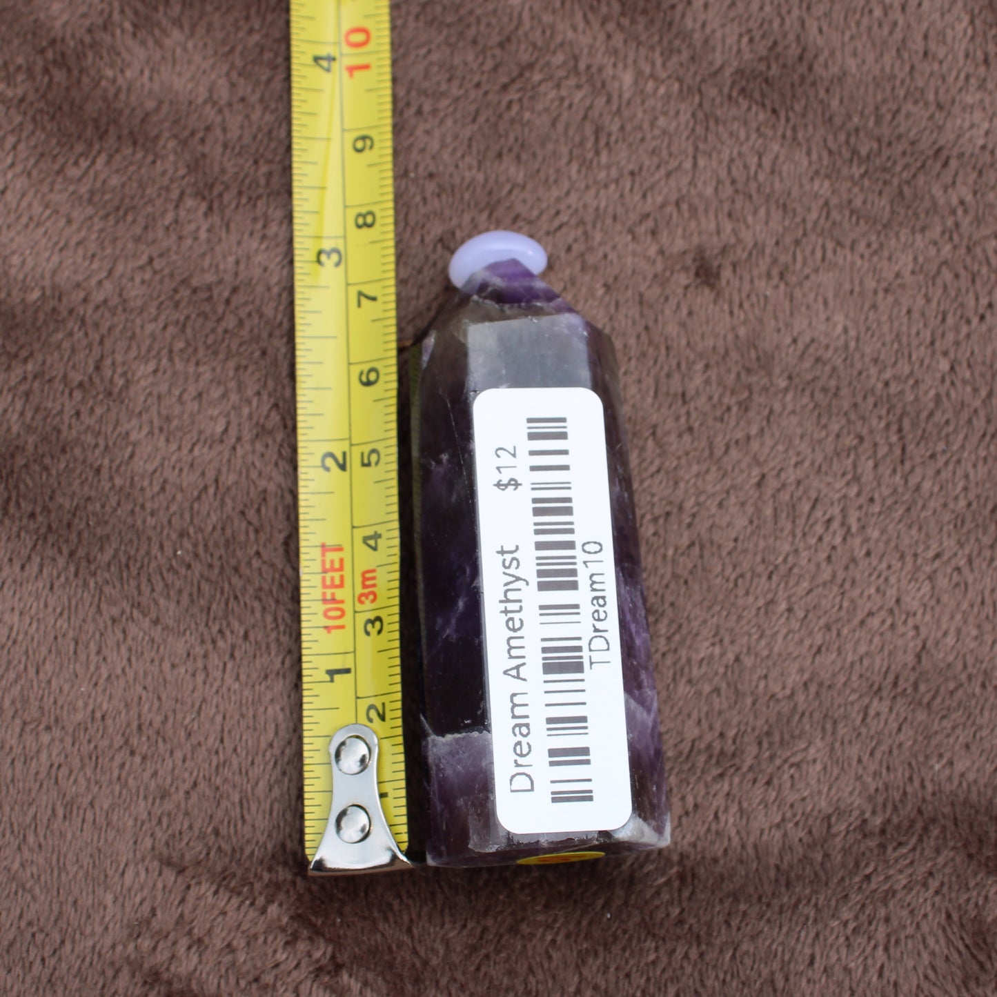 Dream Amethyst Tower crystal standing next to a yellow measuring tape on brown fabric background