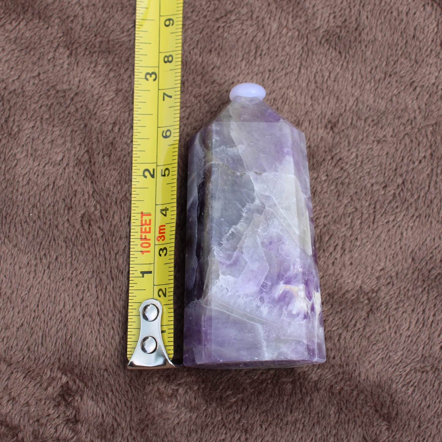 Dream Amethyst Tower crystal with purple and white hues next to yellow measuring tape on brown surface