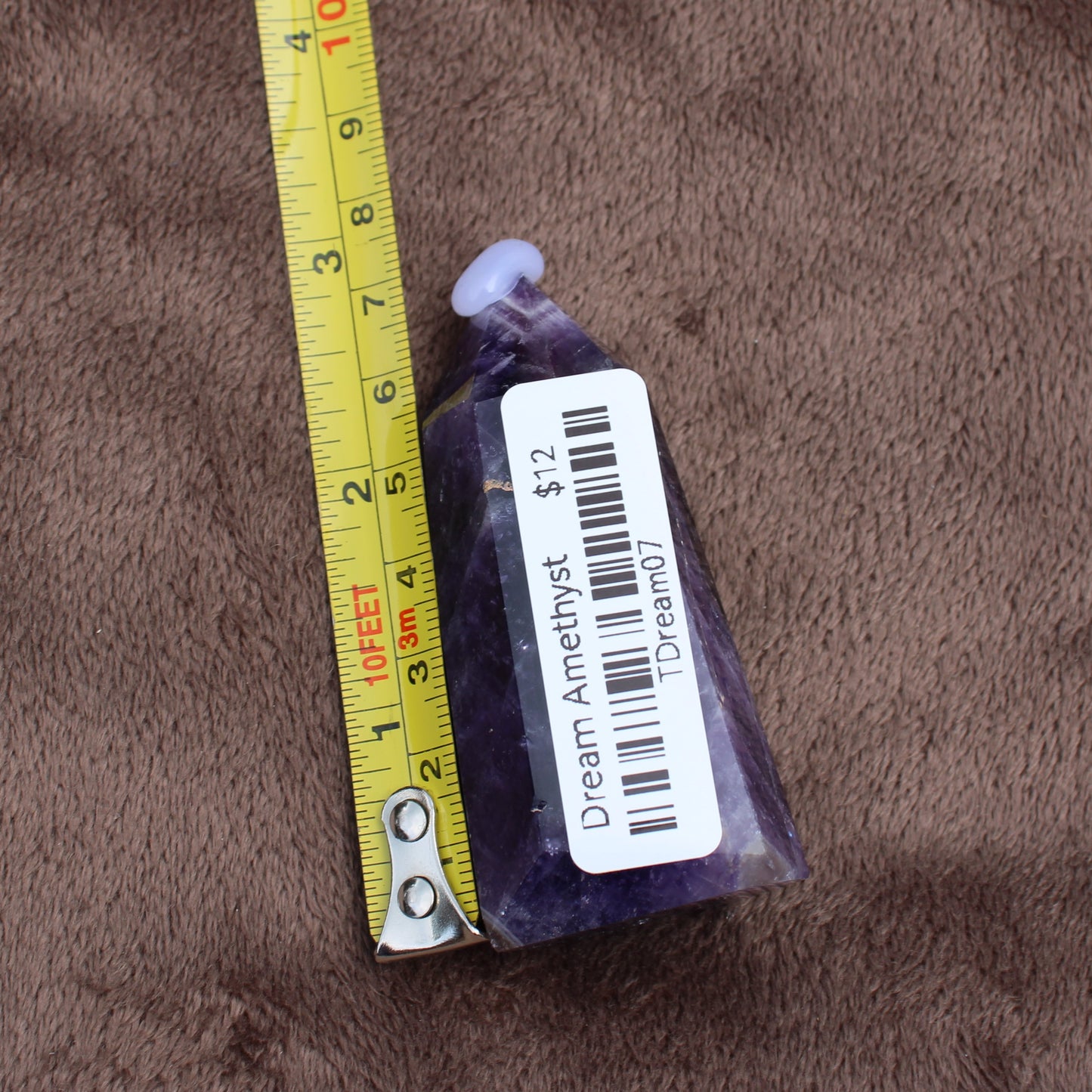Dream Amethyst Tower crystal with measuring tape on brown fabric background by Different Branches LLC