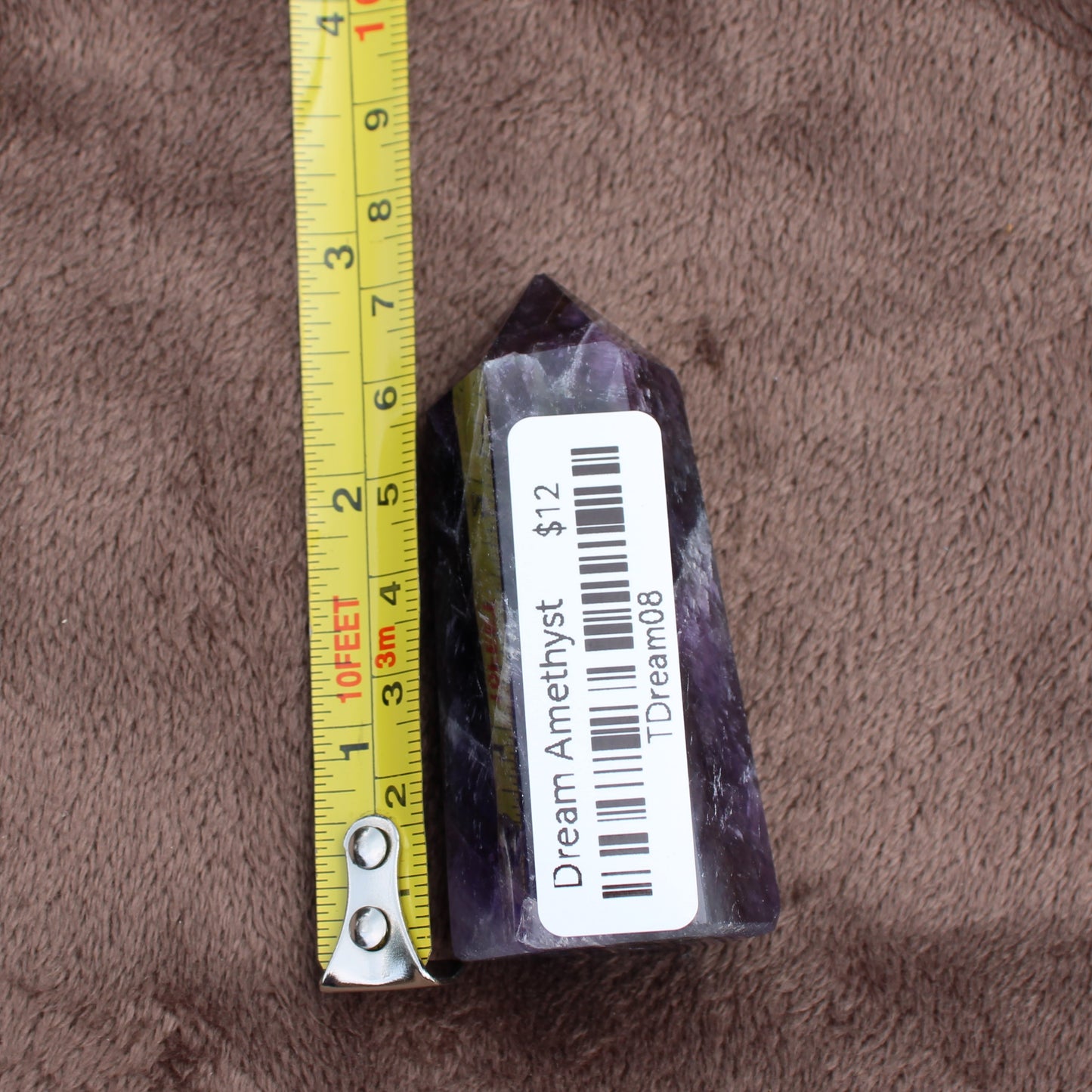 Dream Amethyst Tower crystal next to a yellow measuring tape showing 3 inches tall