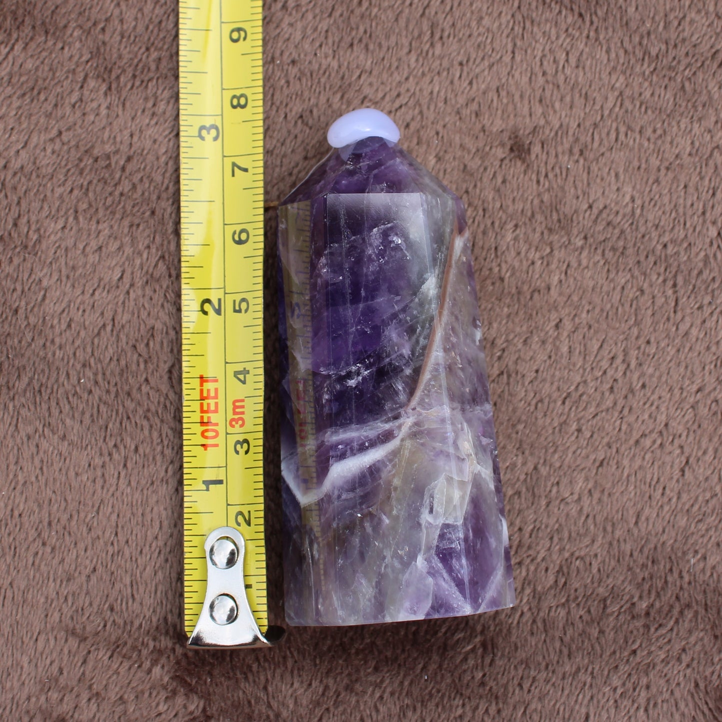 Dream Amethyst Tower crystal standing next to measuring tape on brown fabric background
