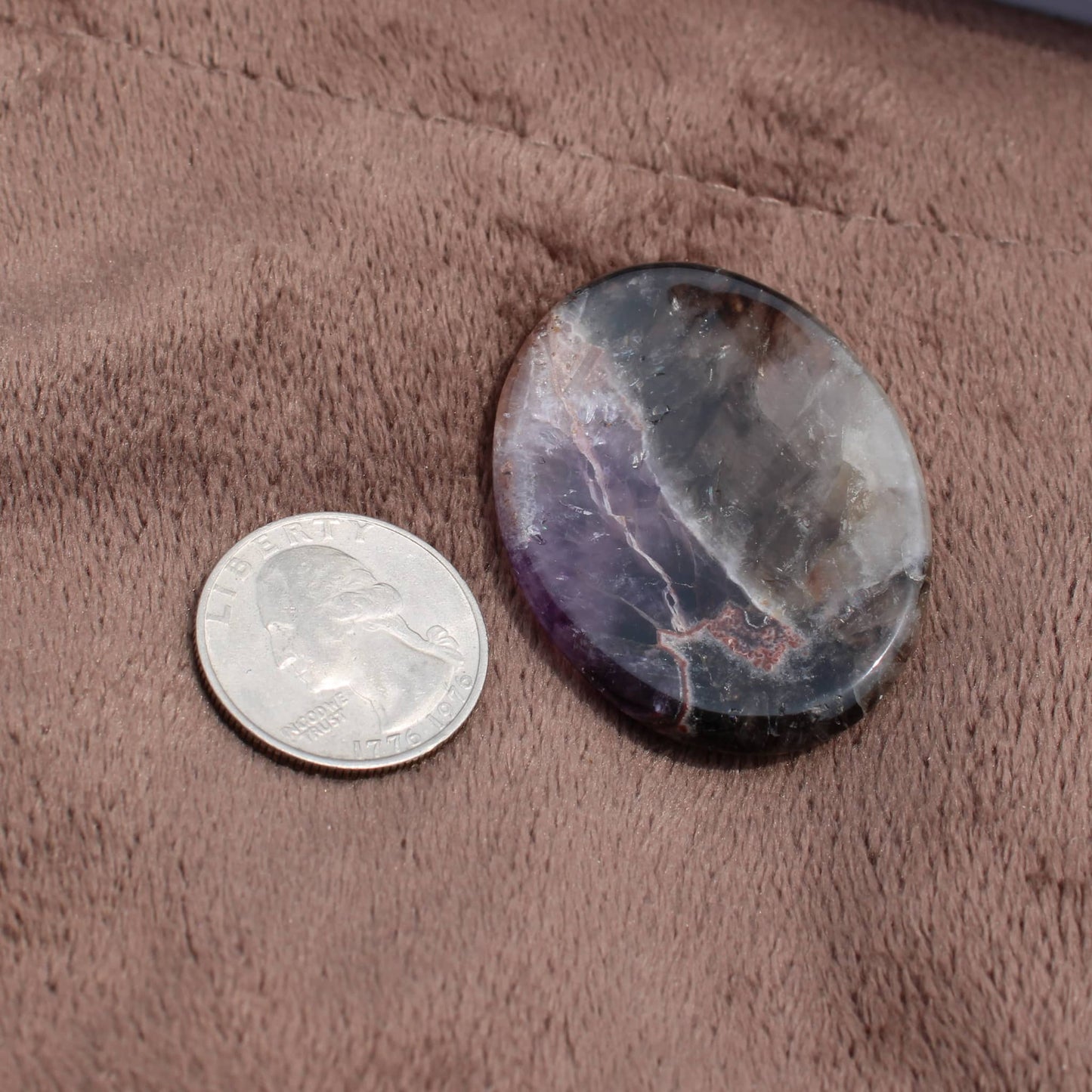 Dream Amethyst Worry Stone next to a US quarter on soft brown fabric for size comparison