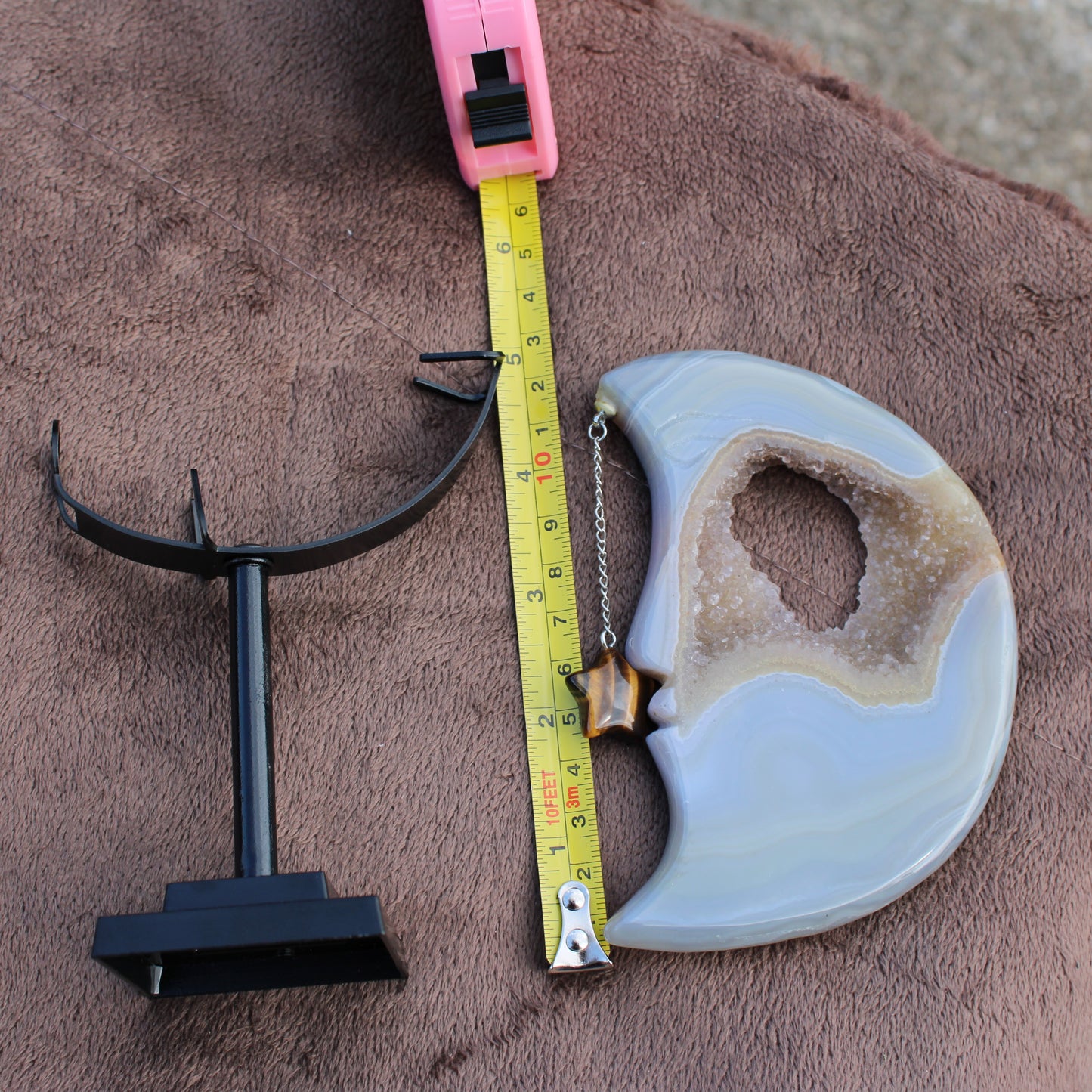 Druzy Agate Moon crystal with metal star pendant and black display stand on brown fabric by Different Branches LLC