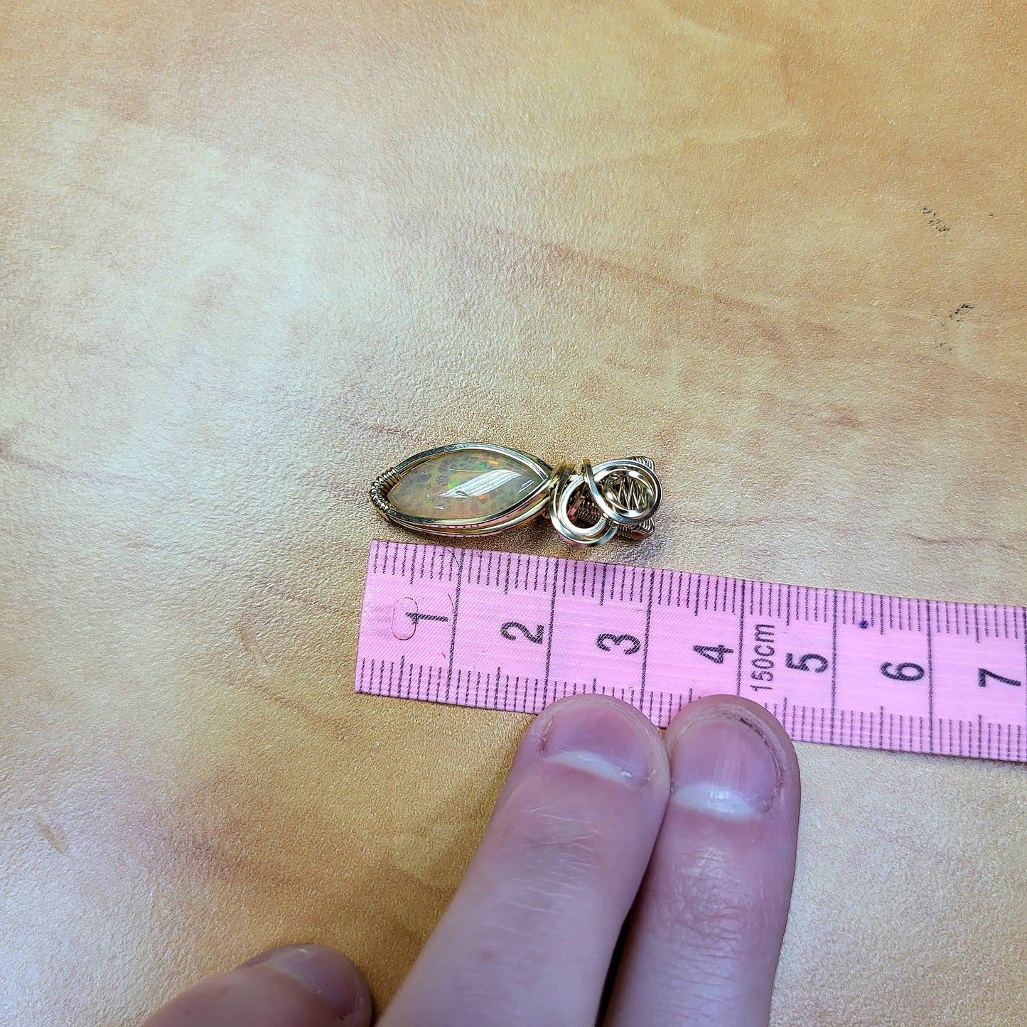 Ethiopian Opal 14k gold-filled pendant on a wooden surface with measuring tape for size reference