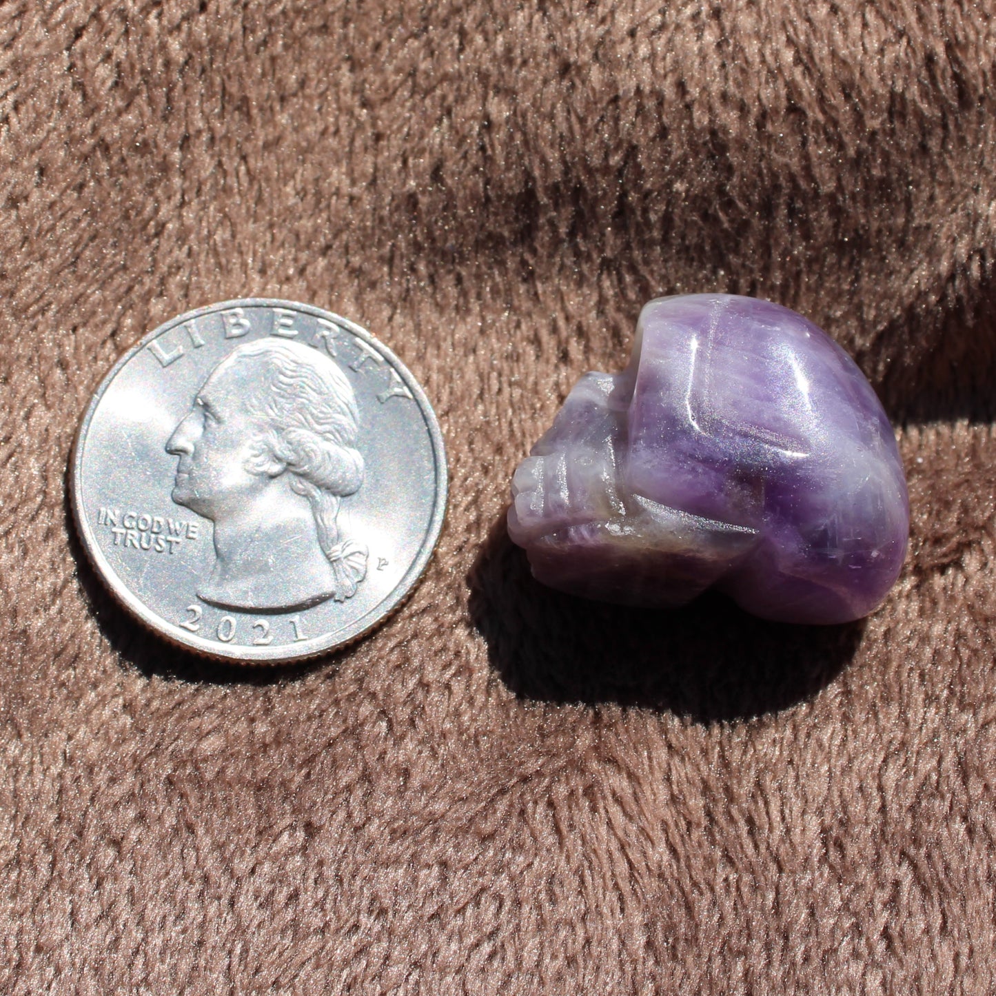 Gemstone Sugar Skull Carvings in Amethyst next to a quarter for size comparison